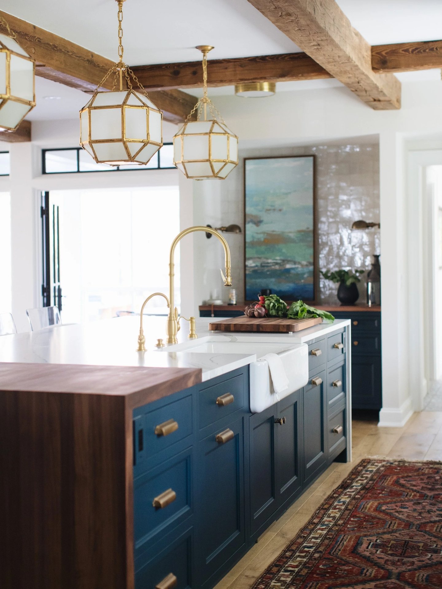 This kitchen is a master class in cabinetry and proportion. The deep navy island carries full inset doors, oversized hardware for comfortable grip, and a walnut waterfall that ties into the ceiling beams. The perimeter stays light so the range wall a