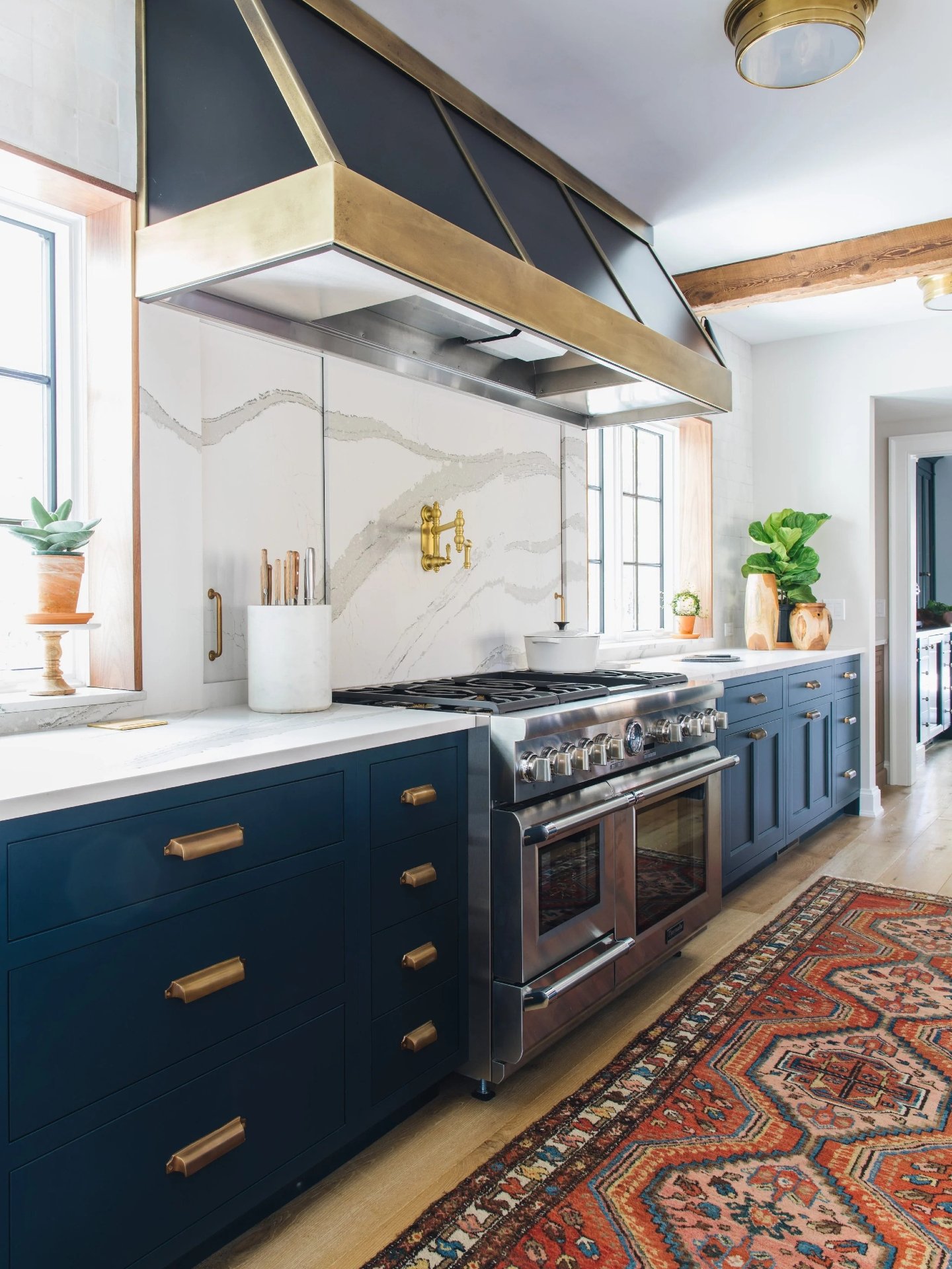 Blue inset cabinetry, brass fixtures, and a waterfall stone island that actually works as hard as it looks. Hidden storage built into both sides keeps the prep zone clean and the counters clear. Which detail grabs you? The beams, the brass, or the is