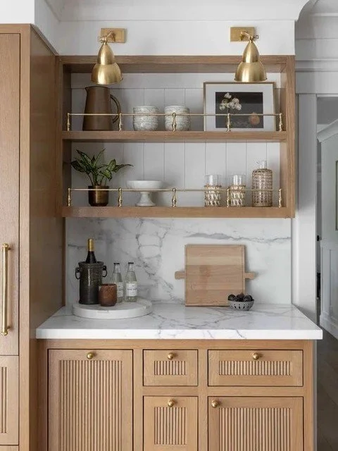 This built in blends closed storage, open shelving, and integrated wine refrigeration into one cohesive wall. Fluted drawer fronts add texture, while brass accents bring warmth and balance. Every detail is planned so the cabinetry feels architectural