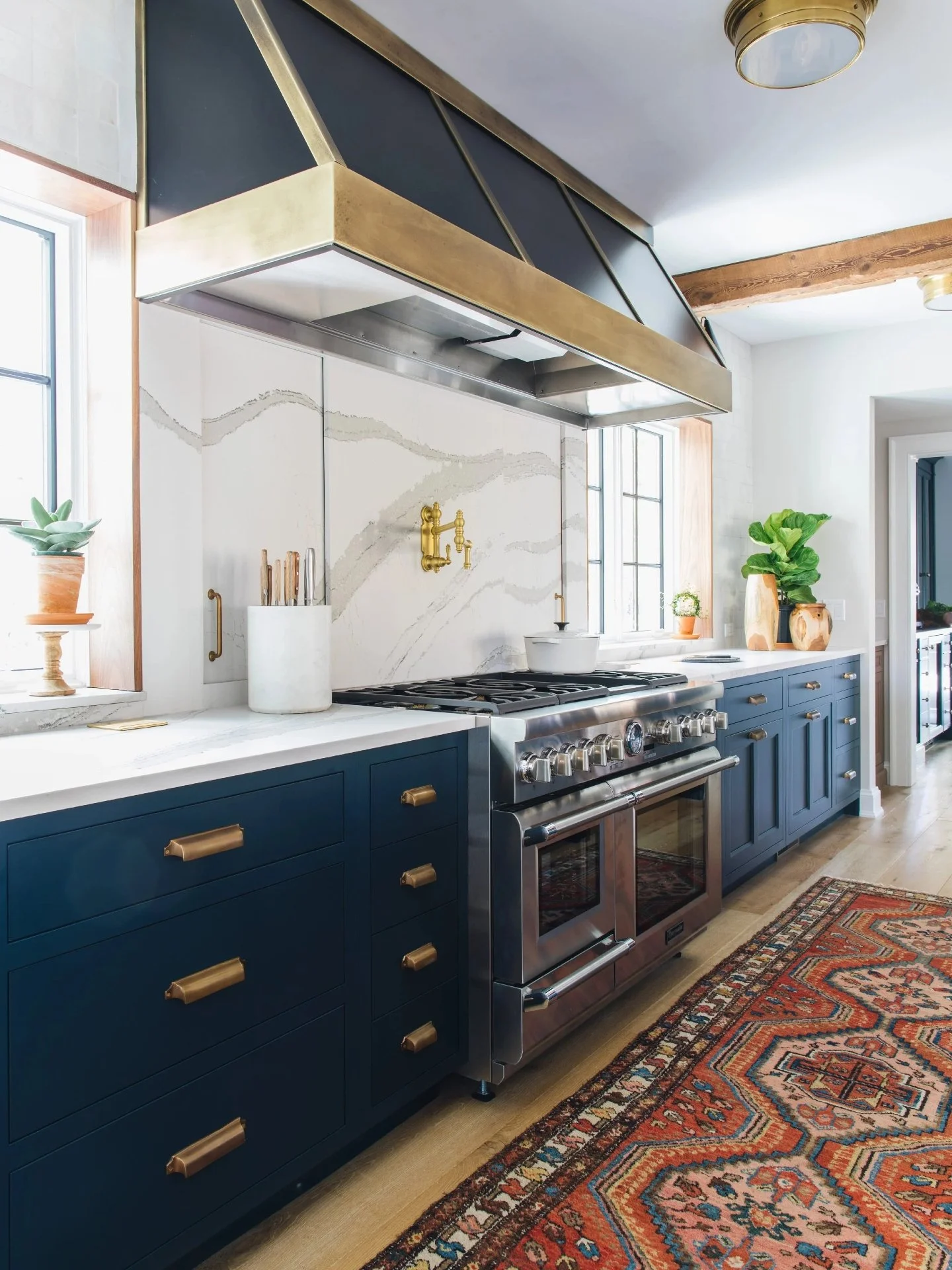 Blue inset cabinetry, brass fixtures, and a waterfall stone island that actually works as hard as it looks. Hidden storage built into both sides keeps the prep zone clean and the counters clear. Which detail grabs you? The beams, the brass, or the is