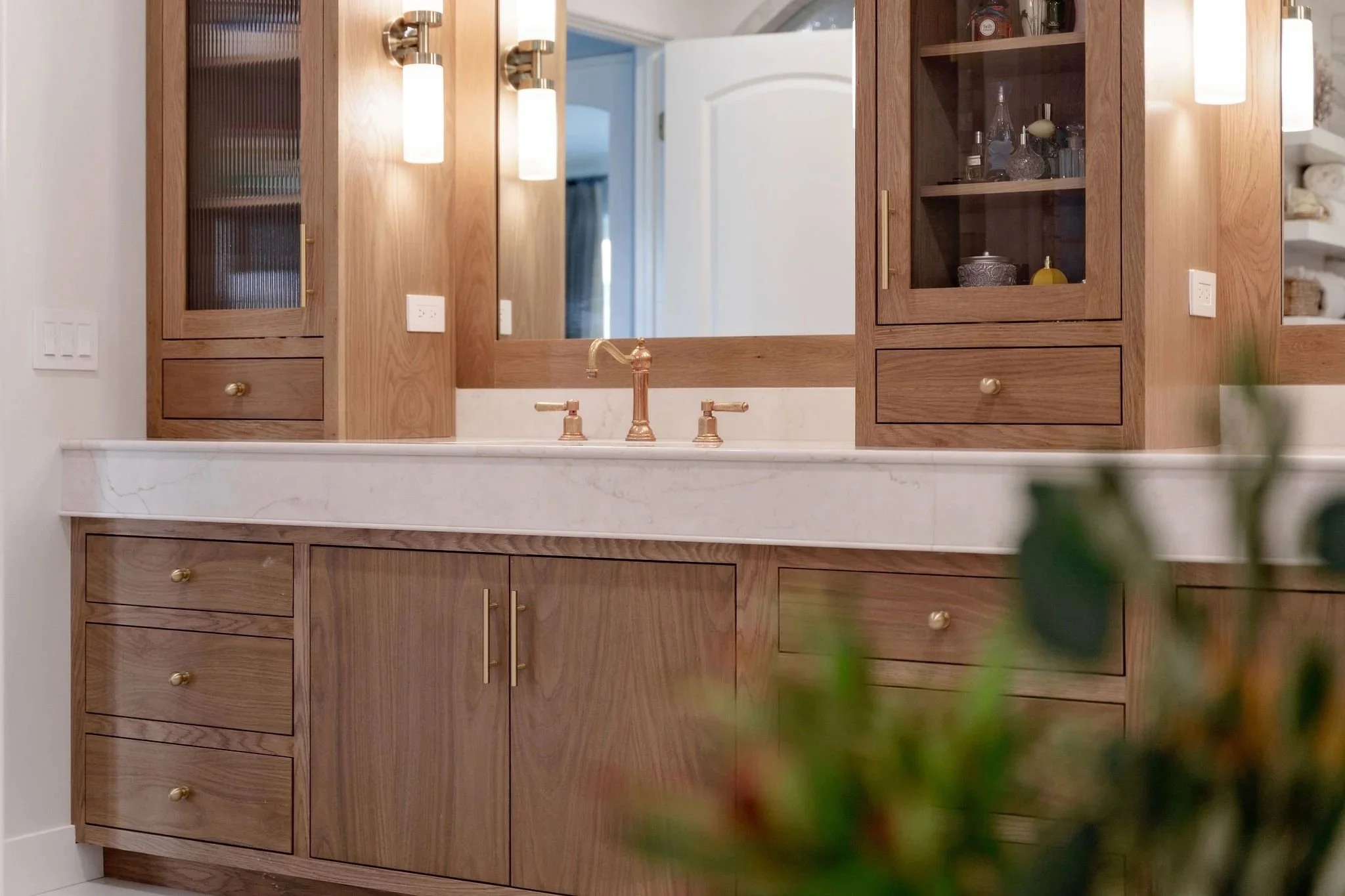 Shaker style bathroom vanity cabinetry with warm wood cabinet doors, integrated drawers, brass hardware, marble countertop, and glass front storage, showcasing timeless bathroom cabinetry design.