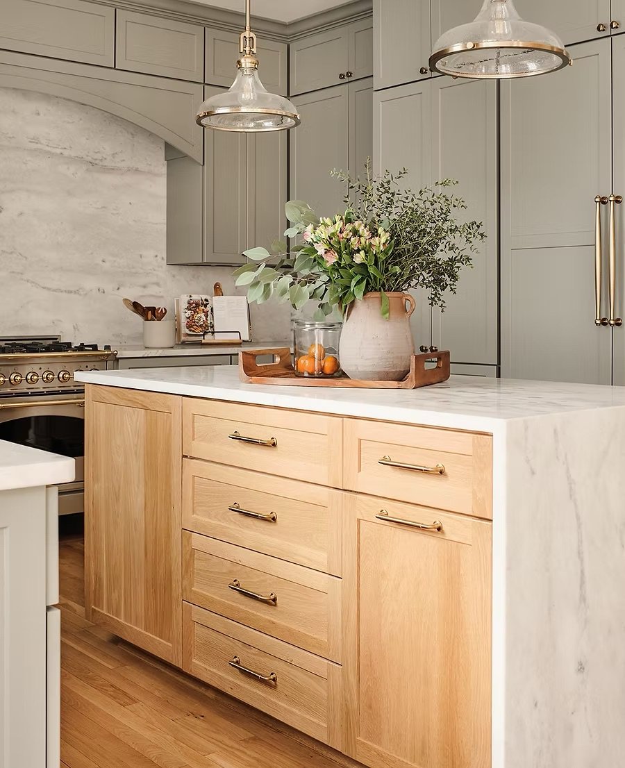 Kitchen with warm wood cabinetry, soft painted cabinets, brass hardware, and layered natural materials representing timeless kitchen design trends for 2026.