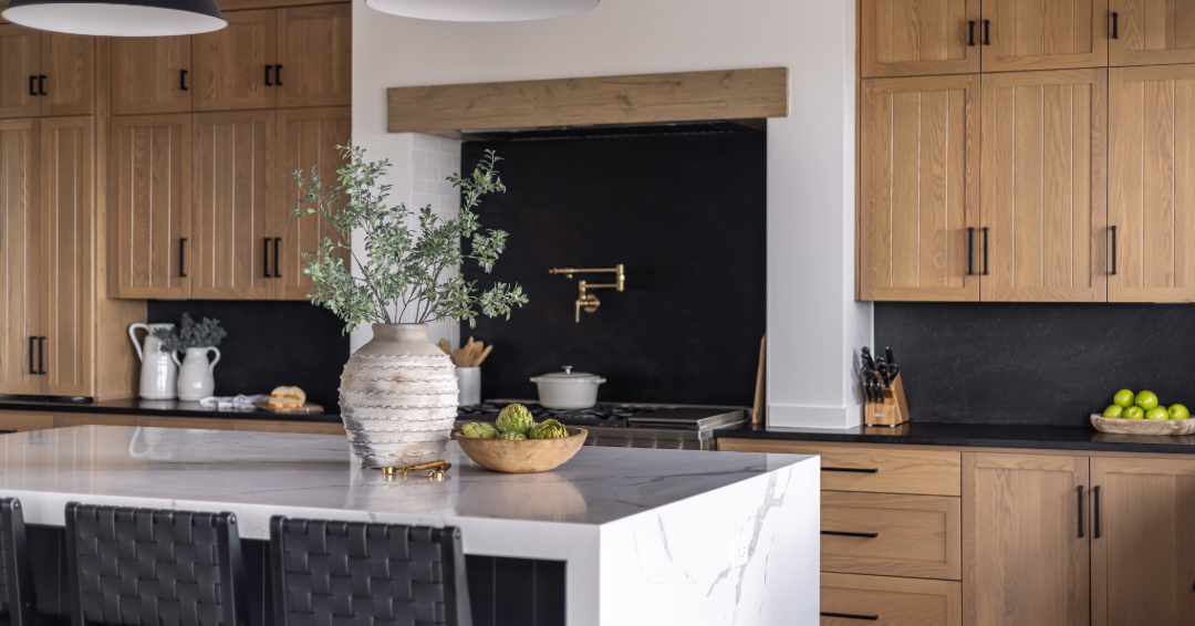 Light oak kitchen cabinets with matte black hardware and a clean modern range hood in a bright natural kitchen.