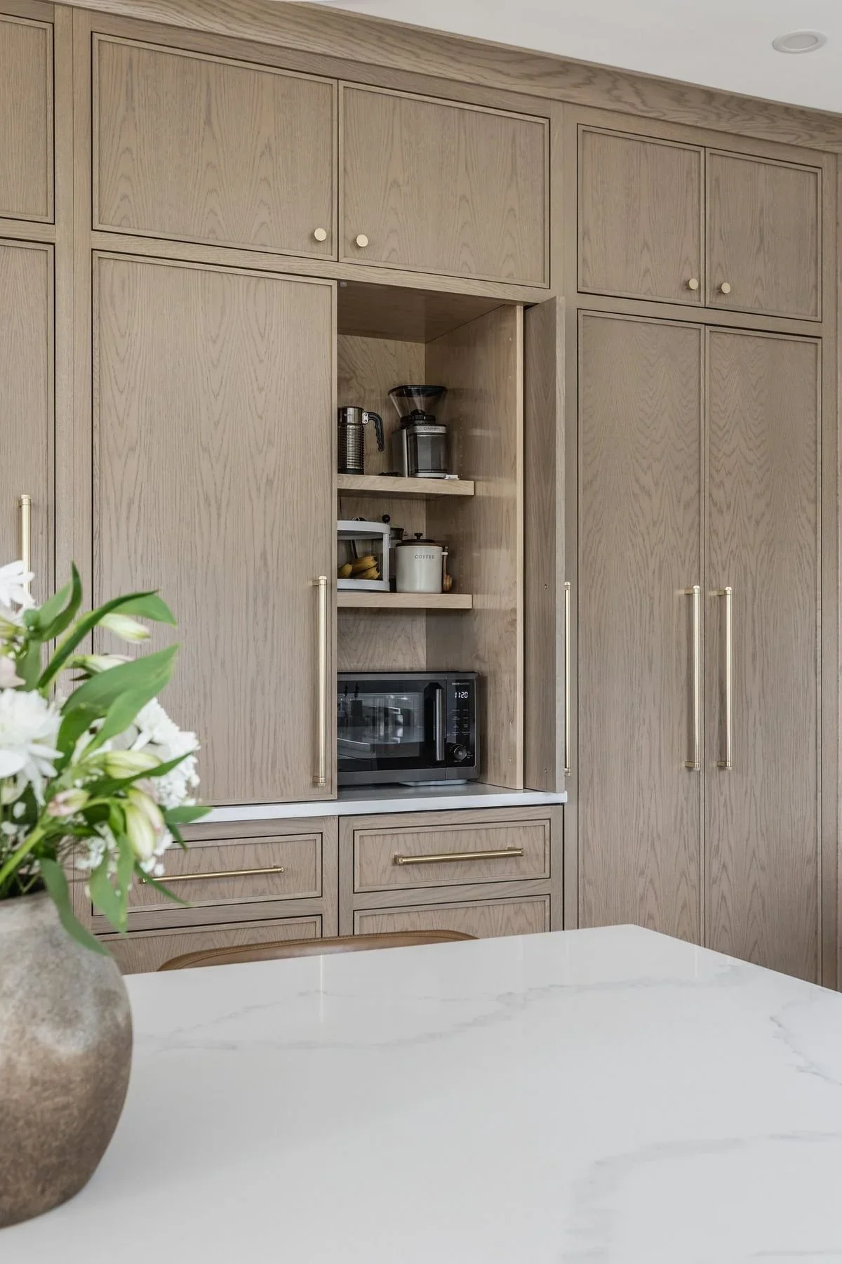 Bright white shaker kitchen with black pendant lighting and oversized island representing the repetitive builder-grade kitchen trend seen in many new homes.