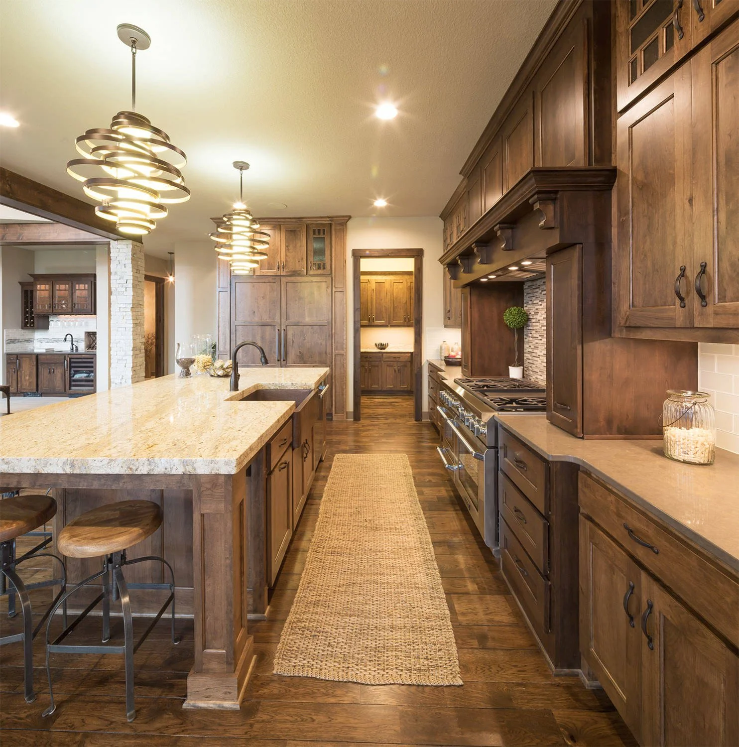 Warm walnut kitchen cabinets with oversized island, natural wood finishes, woven runner rug, and layered lighting in a timeless luxury kitchen design with custom cabinetry and earthy textures