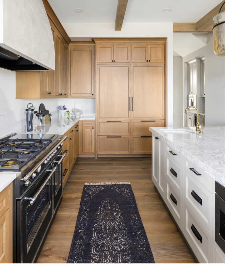 Warm white oak kitchen cabinetry with a painted island, quartz countertops, brass fixtures, and natural wood accents, showcasing contemporary cabinet design that balances warmth and timeless style.