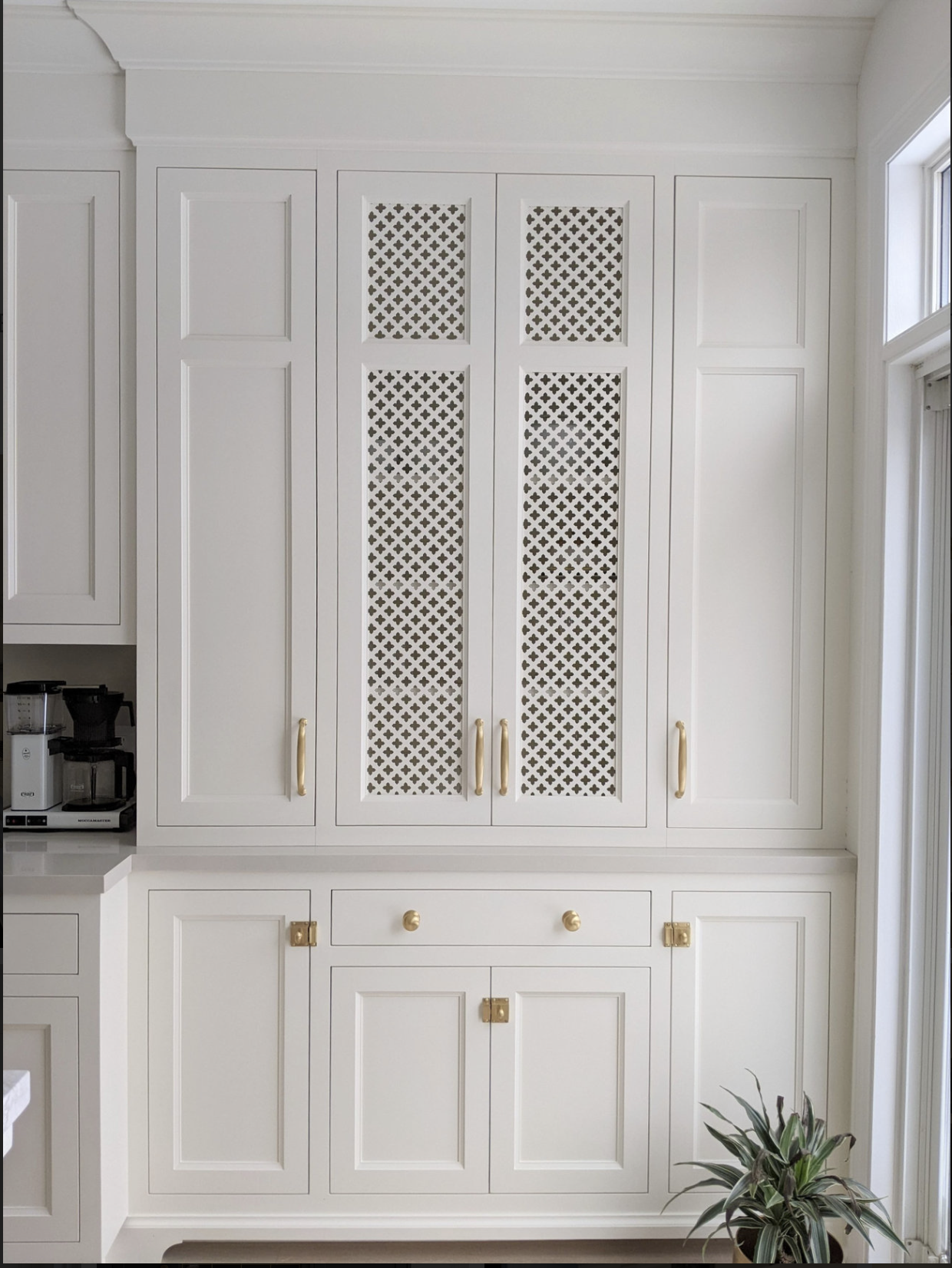 White custom cabinetry with decorative perforated cabinet panels and brass hardware, showcasing detailed millwork and craftsmanship by Bloomsbury Fine Cabinetry in Toronto.