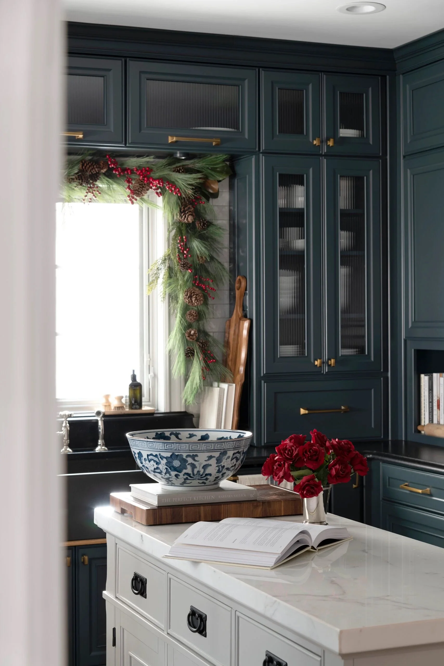Custom kitchen cabinetry with glass-front doors and brass hardware, styled for Christmas with greenery and seasonal decor, highlighting timeless craftsmanship by a professional cabinetry company in Georgia.