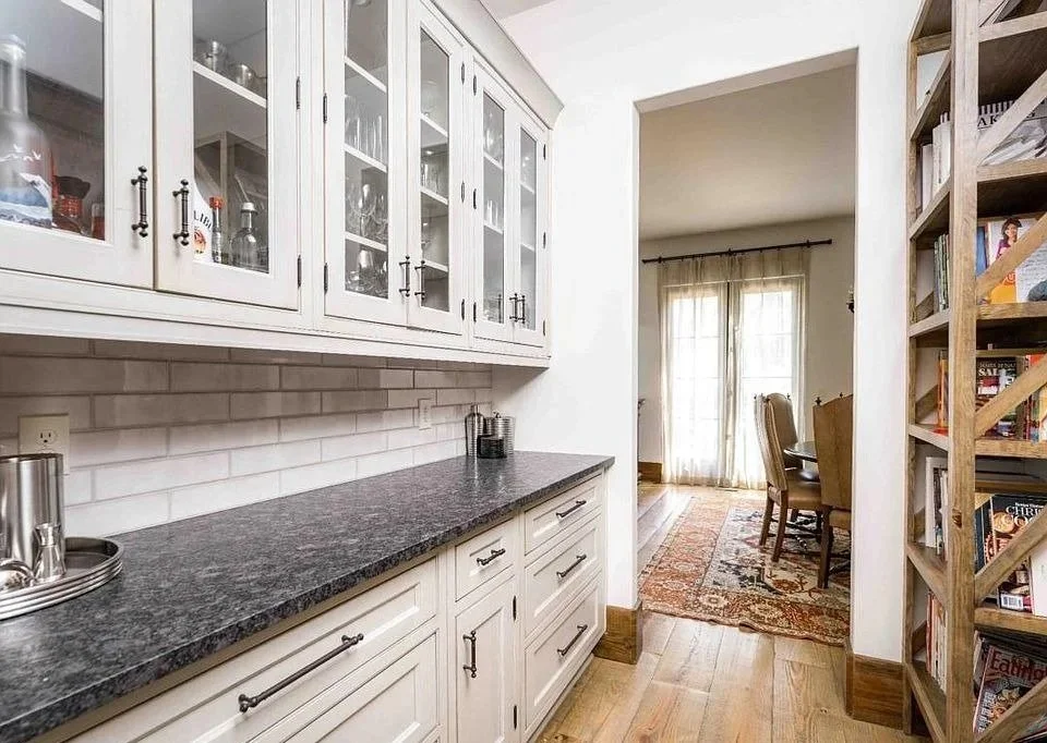 Butler’s pantry with white glass-front cabinets, dark countertops, and tall open pantry shelving.