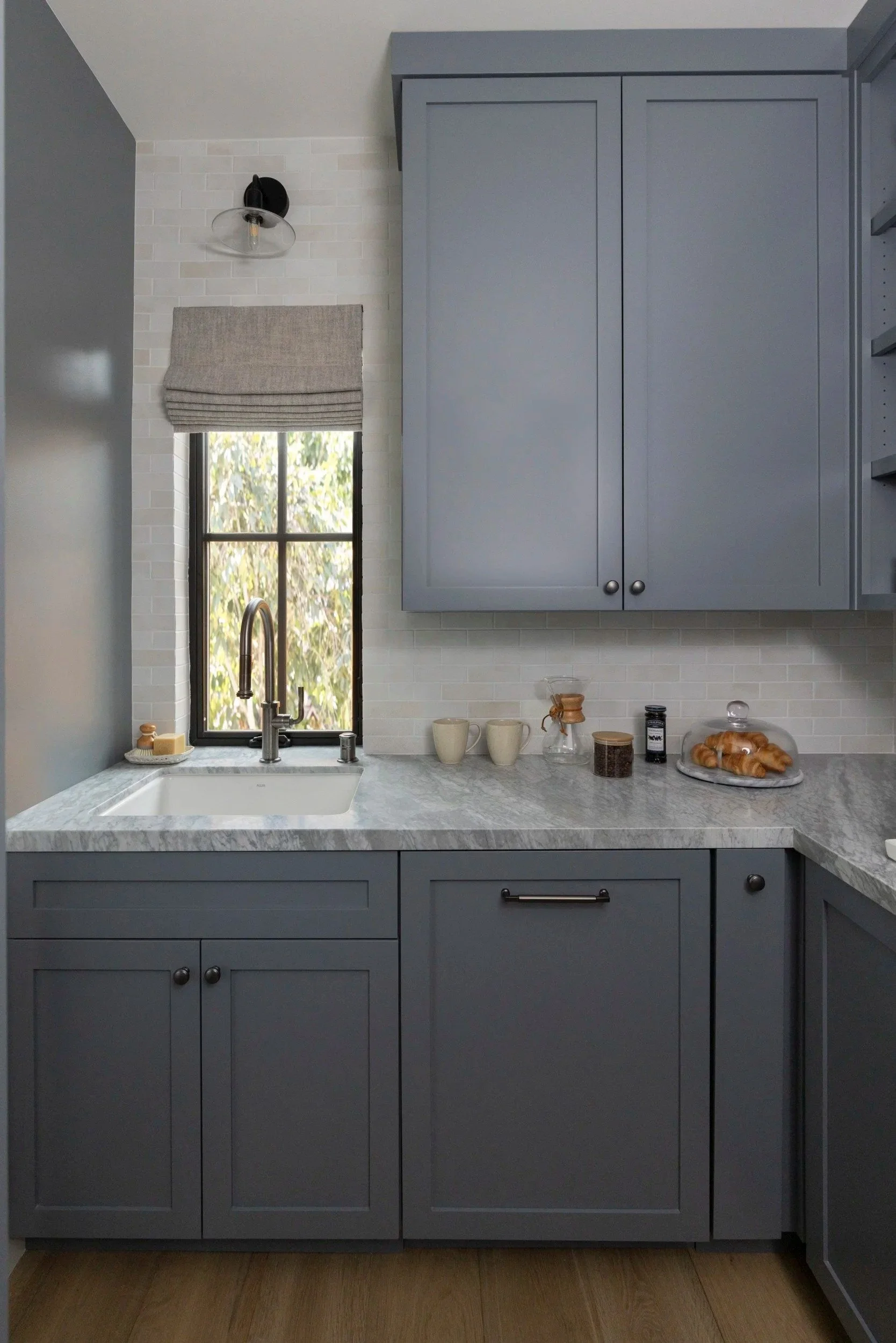 Muted blue-gray kitchen cabinetry with classic door fronts, simple hardware, marble countertops, and a clean, functional layout designed for everyday use.