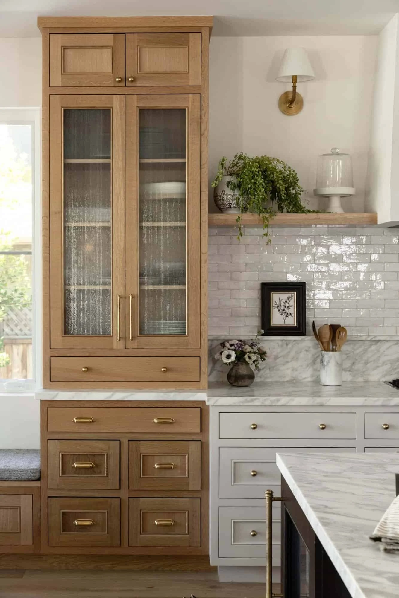Medium oak pantry cabinet with glass cabinet doors, marble countertops, brass hardware, and collected kitchen design details