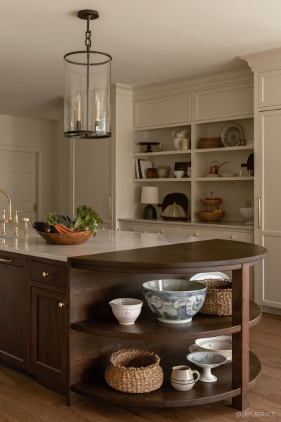 Furniture-inspired walnut kitchen island featuring open display shelving, rich wood tones, brass fixtures, and white countertops, blending classic craftsmanship with modern functionality.