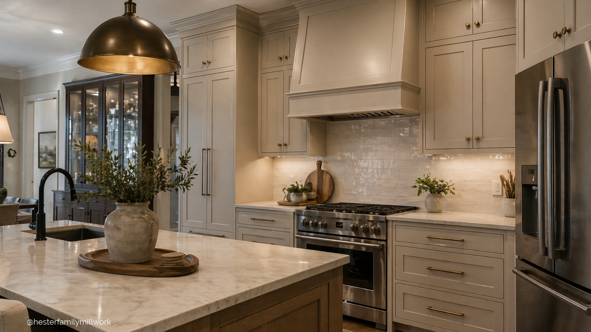Transitional kitchen with taupe painted cabinets, layered lighting, marble countertops, and warm brass hardware creating a refined, cohesive cabinetry design.