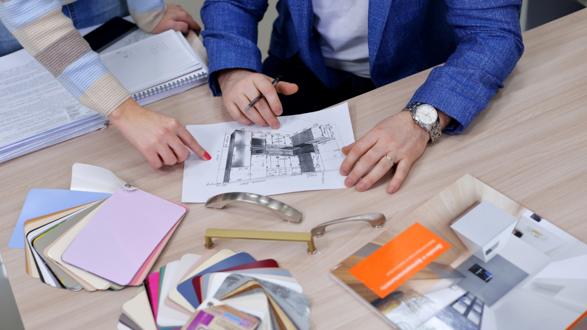 Interior designer reviewing cabinetry hardware samples, color swatches, and floor plans at a design table.
