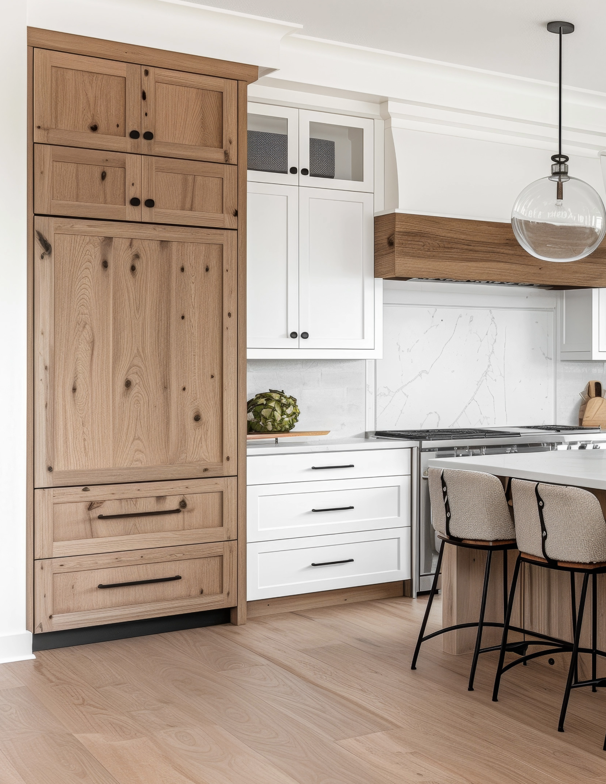 Tall kitchen pantry cabinet in natural wood with black hardware, paired with white shaker cabinets and a wood-wrapped range hood in a bright, modern kitchen.