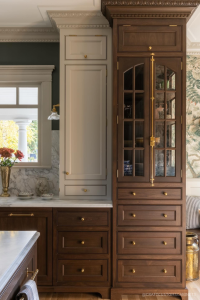 Traditional walnut kitchen cabinetry paired with painted cabinets, decorative crown molding, glass-front storage, and brass hardware, creating a warm and elegant kitchen with timeless appeal.