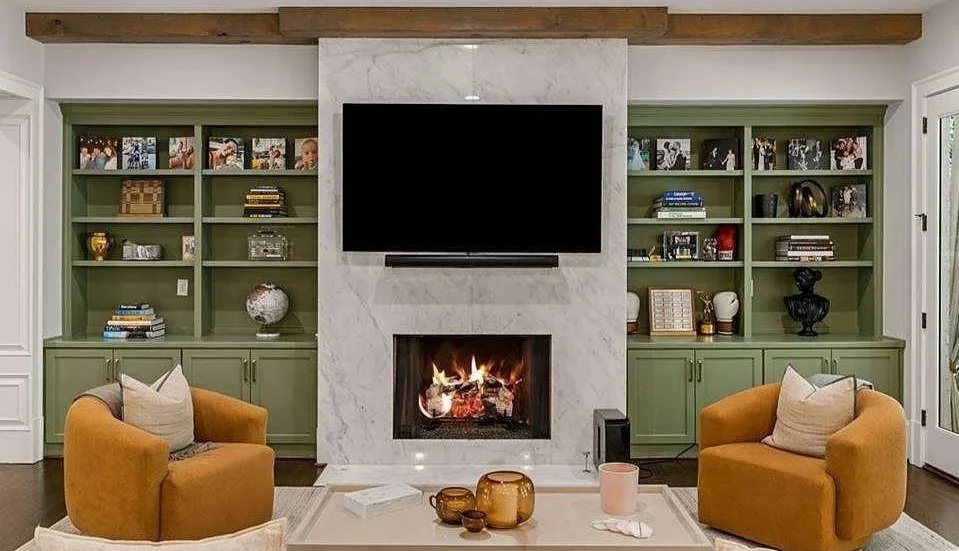 Olive green built-in bookcases flanking a fireplace and television with mustard lounge chairs.