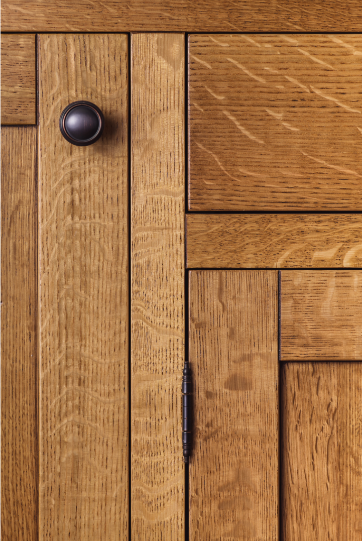 Close up of warm wood cabinetry with a round matte black knob on a raised panel cabinet door.