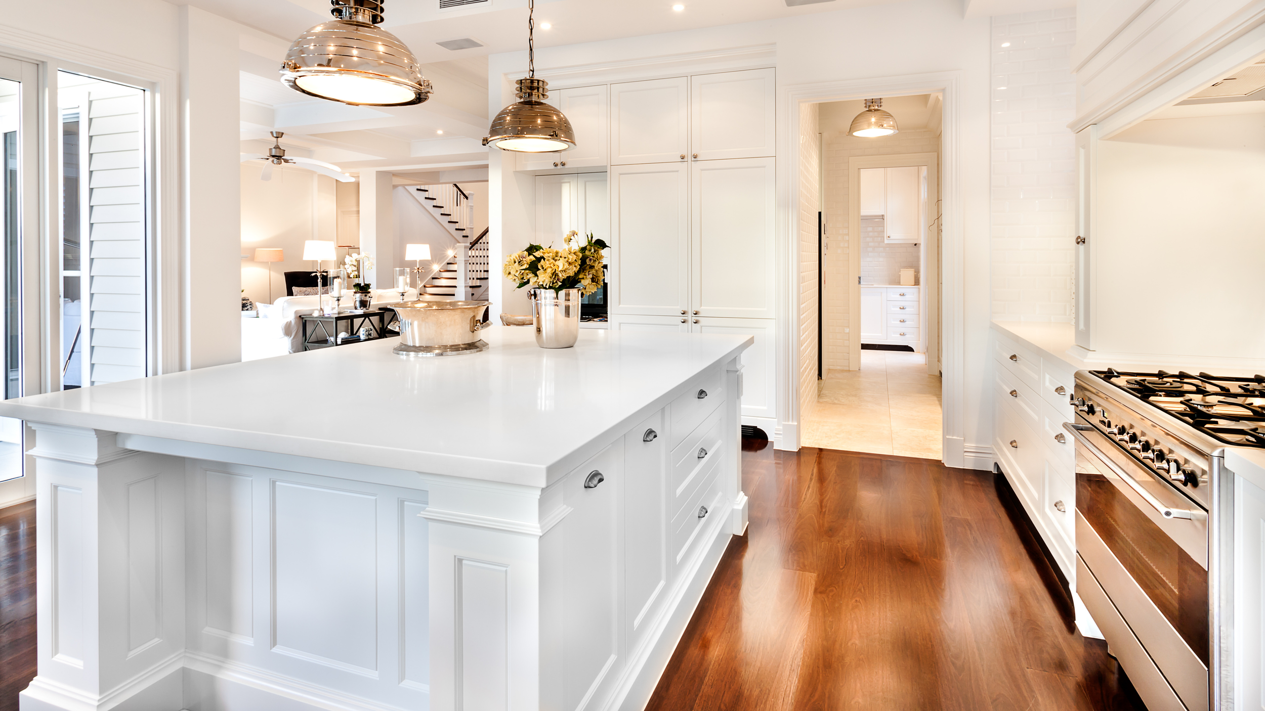 Bright white custom kitchen cabinetry with oversized island, polished chrome pendant lighting, and warm hardwood floors in a timeless luxury kitchen design