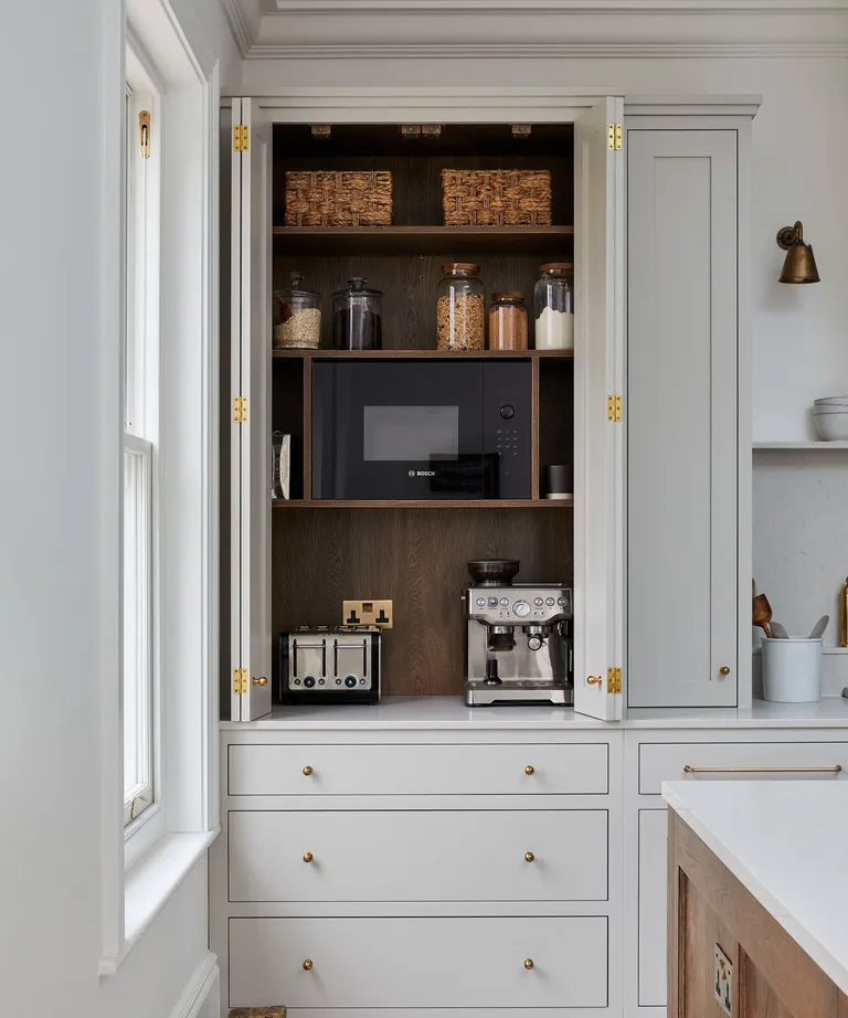 White shaker kitchen cabinets with a hidden appliance garage featuring a wood tambour door, marble countertops, espresso machine, and toaster for a clean, clutter-free kitchen design.