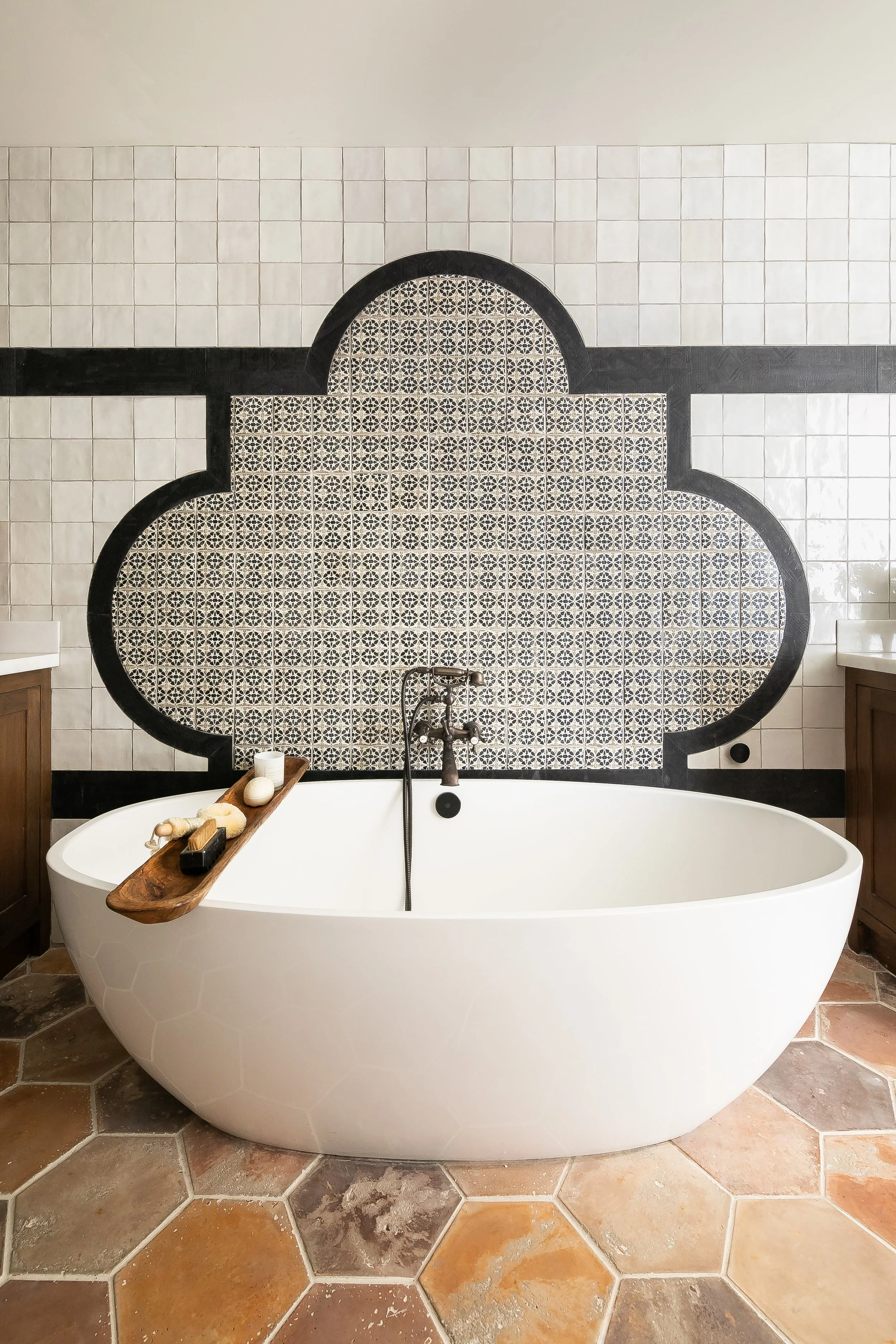 A freestanding oval tub with a Moroccan arabesque tiled on the wall behind it.