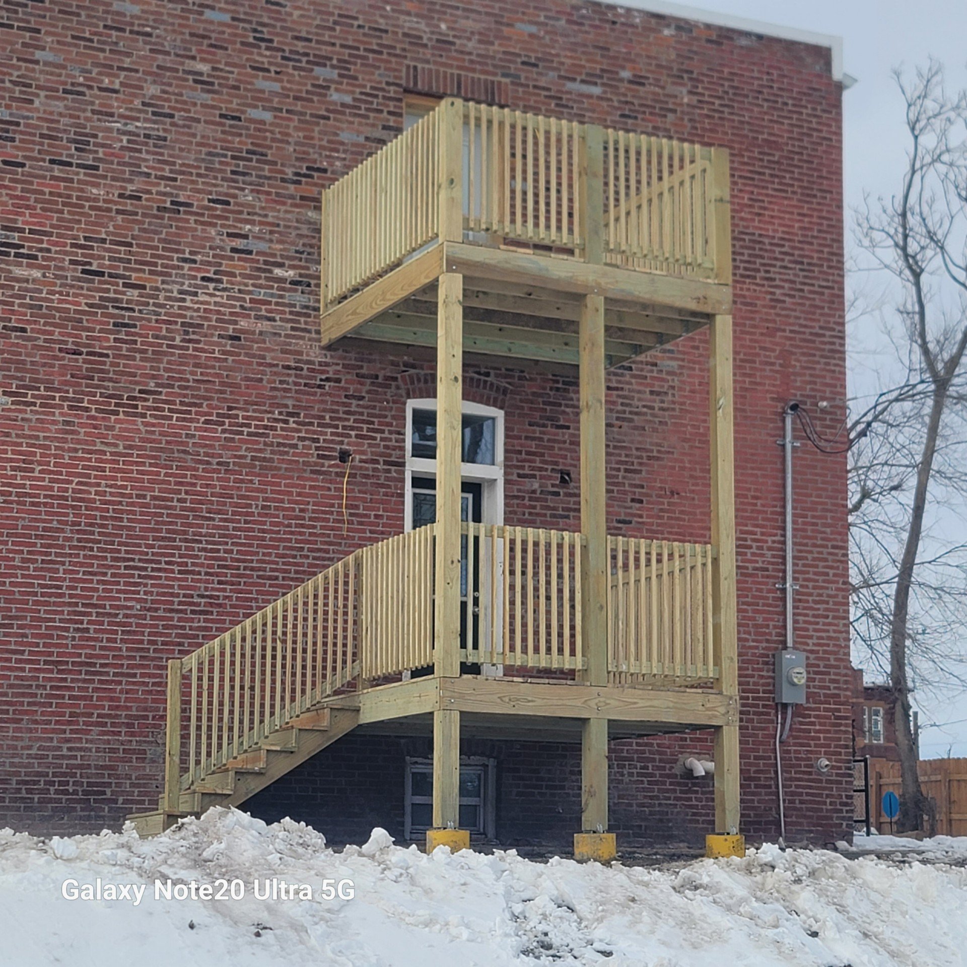 Newly built wooden staircase and balcony attached to a red brick building in snowy weather.