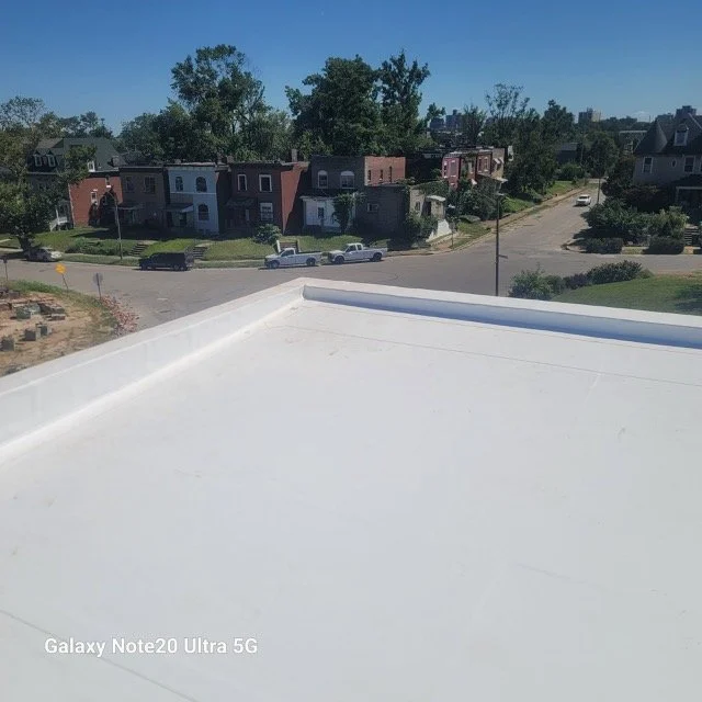 View of residential houses and trees from a rooftop with a clear blue sky.