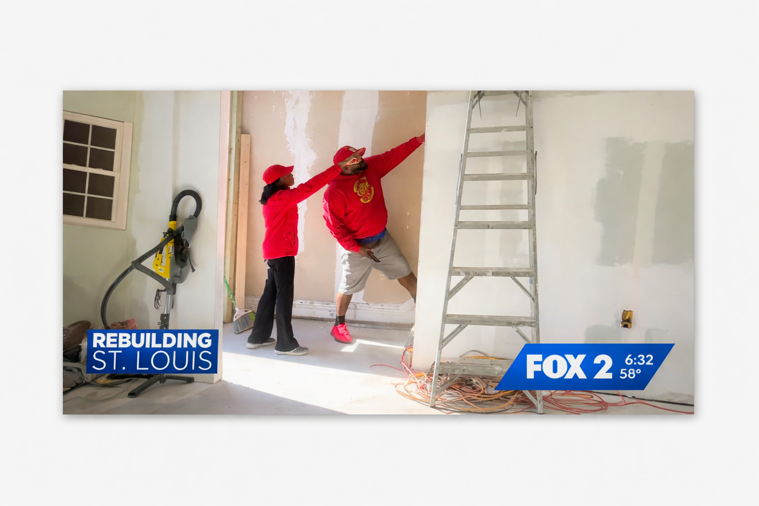 Two construction workers wearing red shirts, red hats, and safety gear working on an unfinished interior wall; one is pointing at the wall while the other looks on, with construction tools and ladder present.