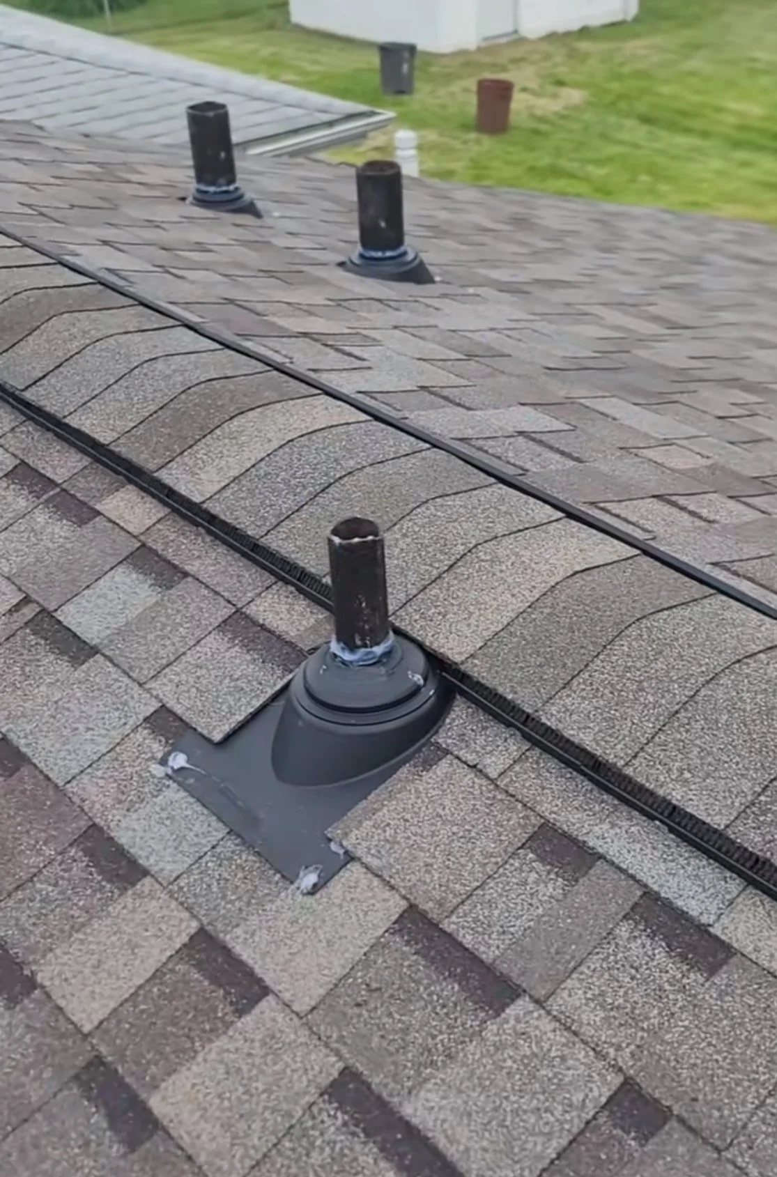 Close-up of a roof with three vent pipes, one of which is poorly installed with its pipe missing, leaving it exposed. The shingles are in good condition.