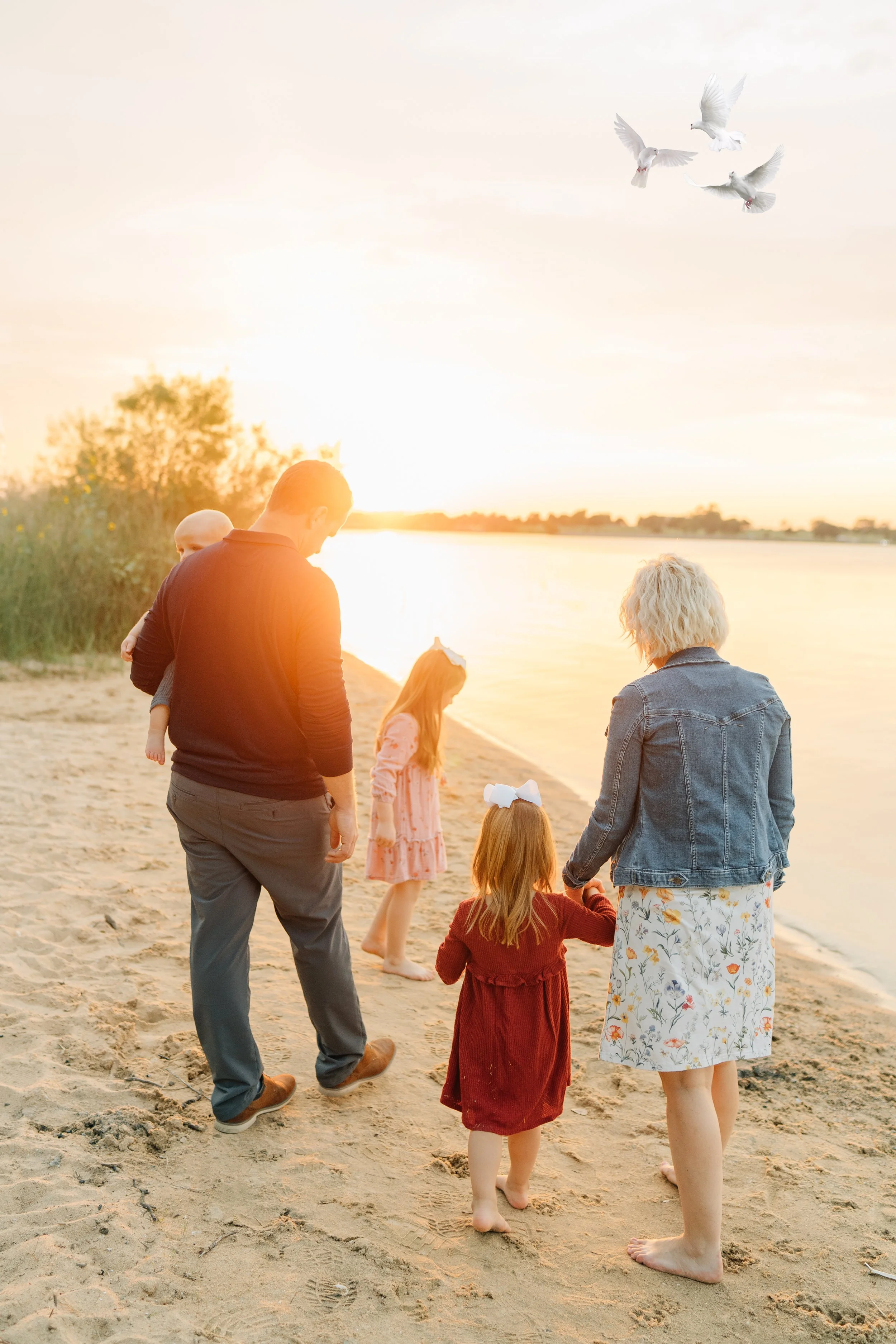 A family of six walking along a sandy beach at sunset, with two white doves flying in the sky.