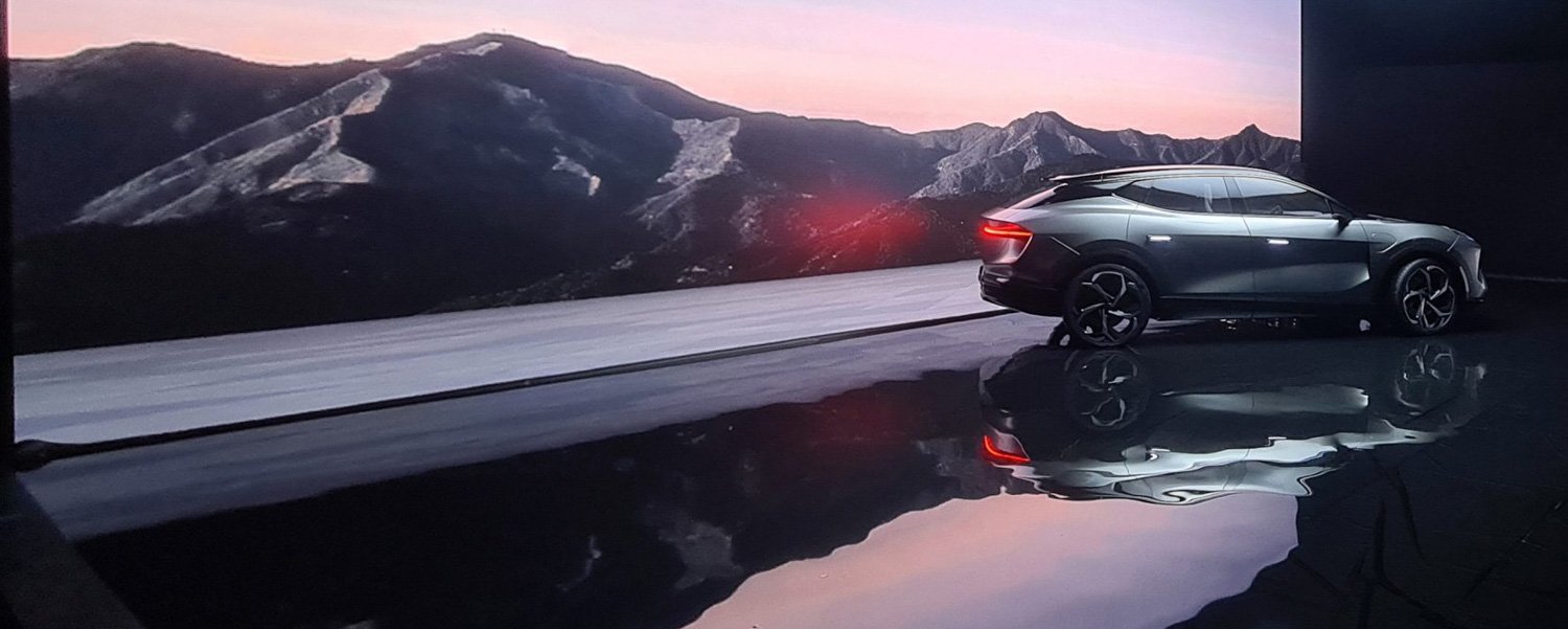 Futuristic gray car parked indoors with a mountain landscape background and reflective floor.