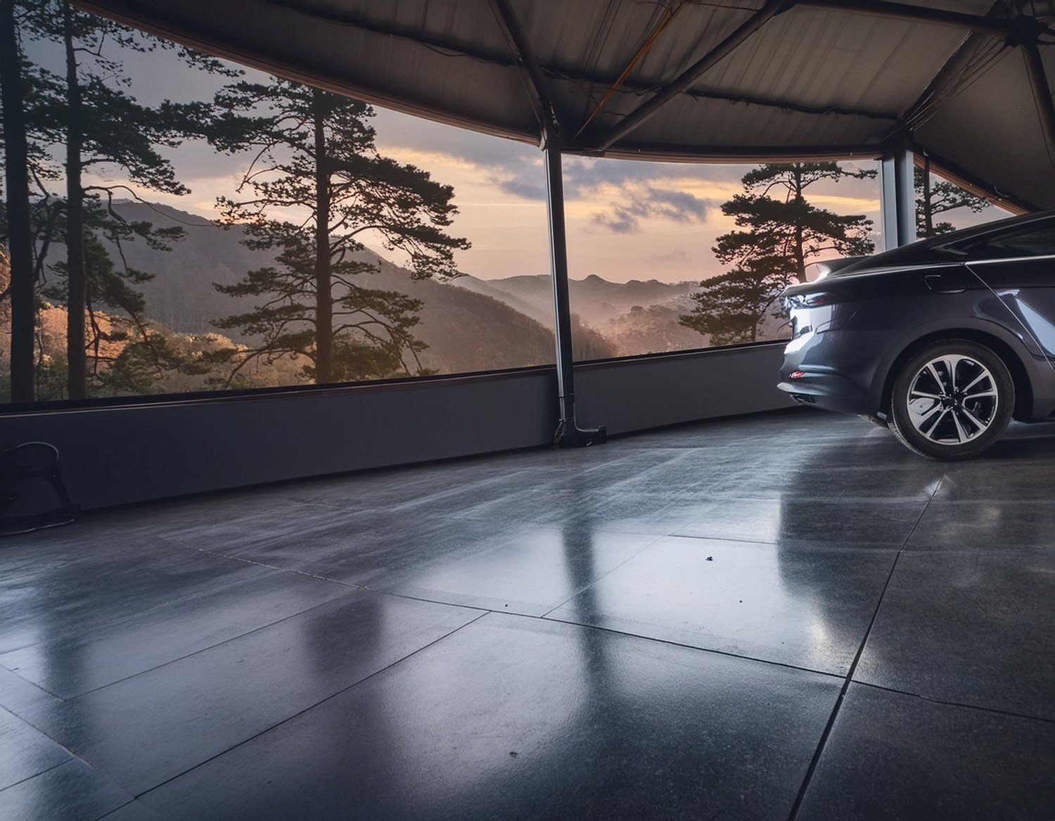 A modern car parked in a garage with large windows, overlooking a scenic view of mountains and trees during sunset.