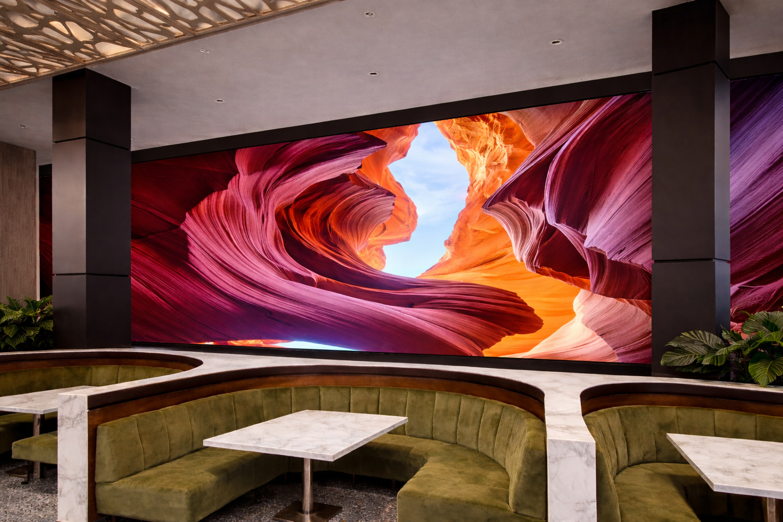 Interior of a modern lounge or restaurant with green velvet banquette seating and white marble tabletops, featuring a large digital mural of Antelope Canyon with red and orange rock formations and a blue sky.