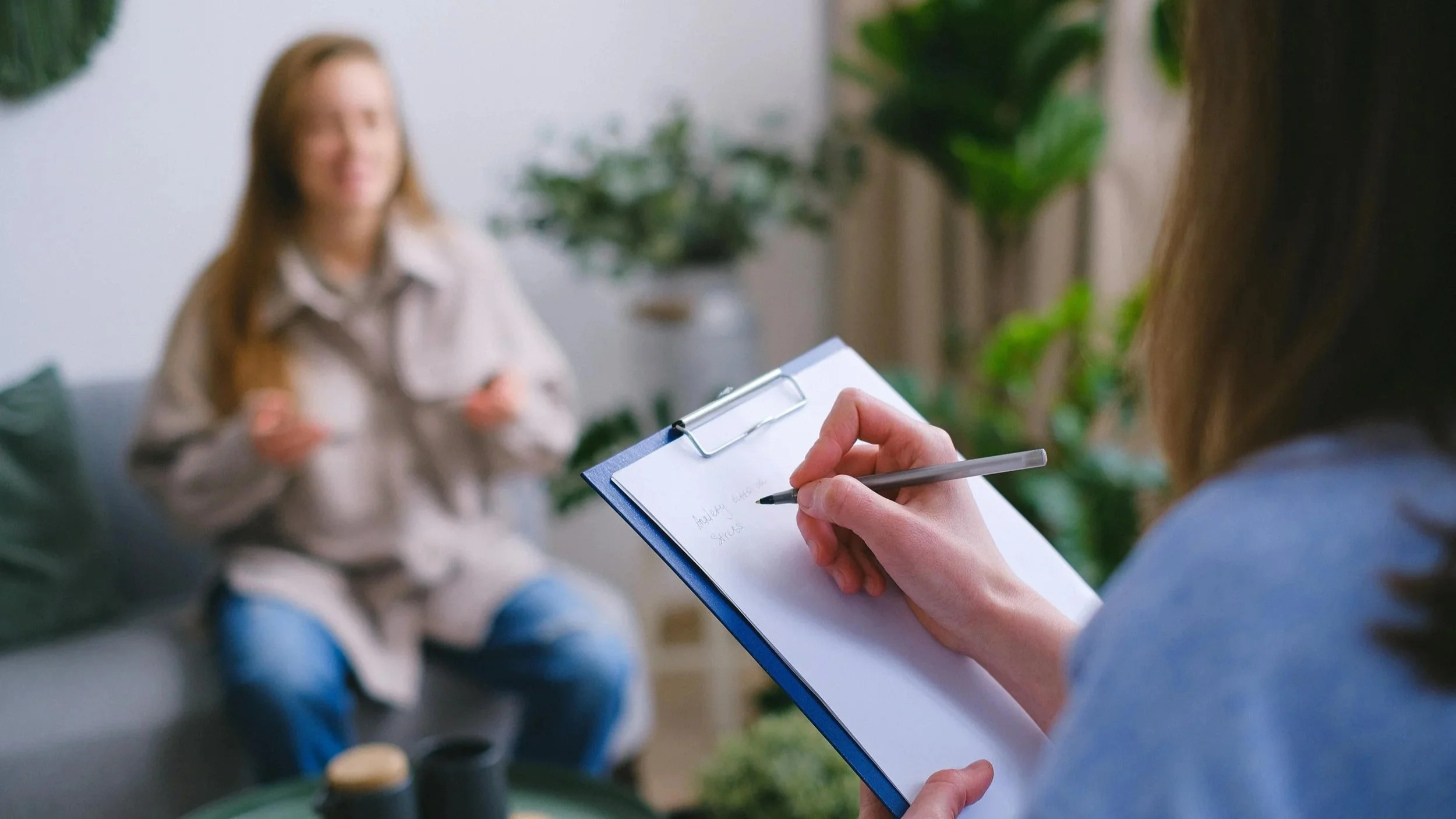 Therapist writing notes on clipboard with a client seated in front