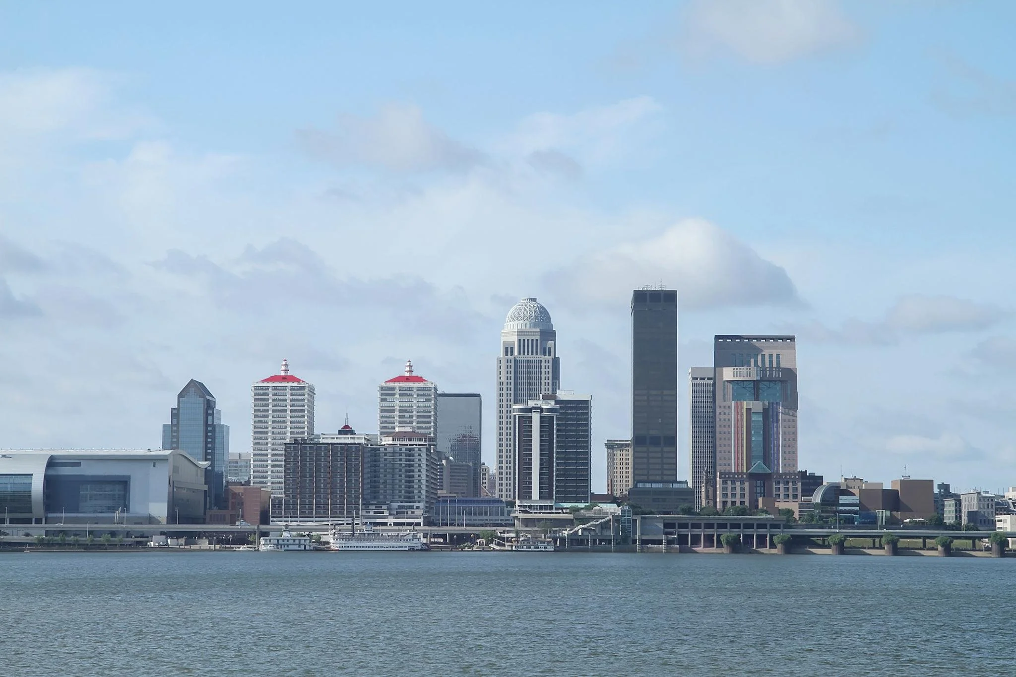 View of a city skyline with several tall skyscrapers and buildings viewed across a body of water under a partly cloudy sky.