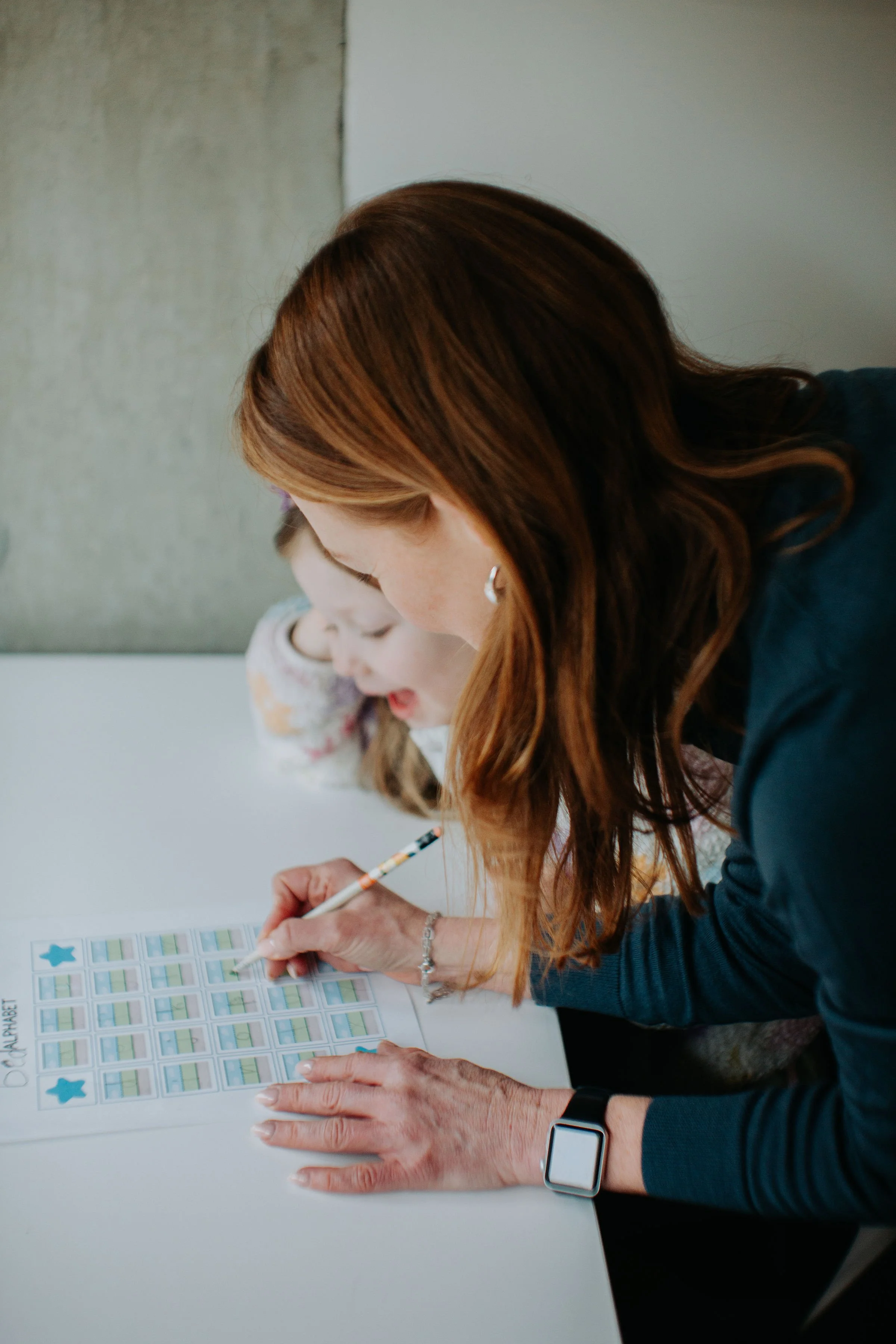 Woman with red hair marking a bingo card with blue star and green grid squares, with a young girl in the background.