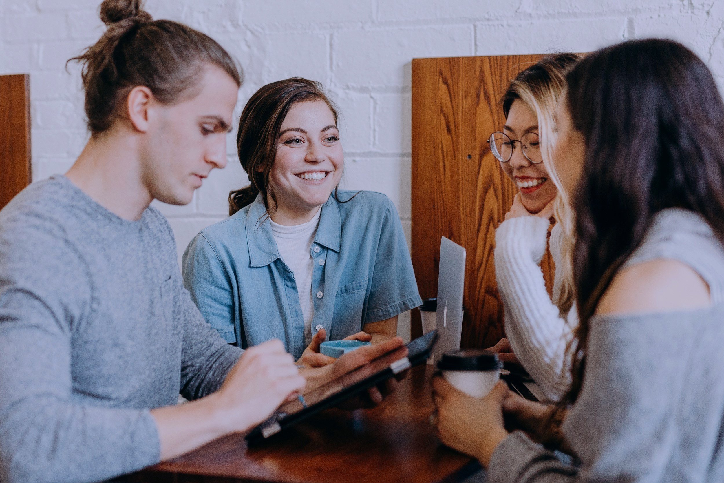 A group of people sitting around a wooden table in a cozy, plant-filled room, engaged in conversation.