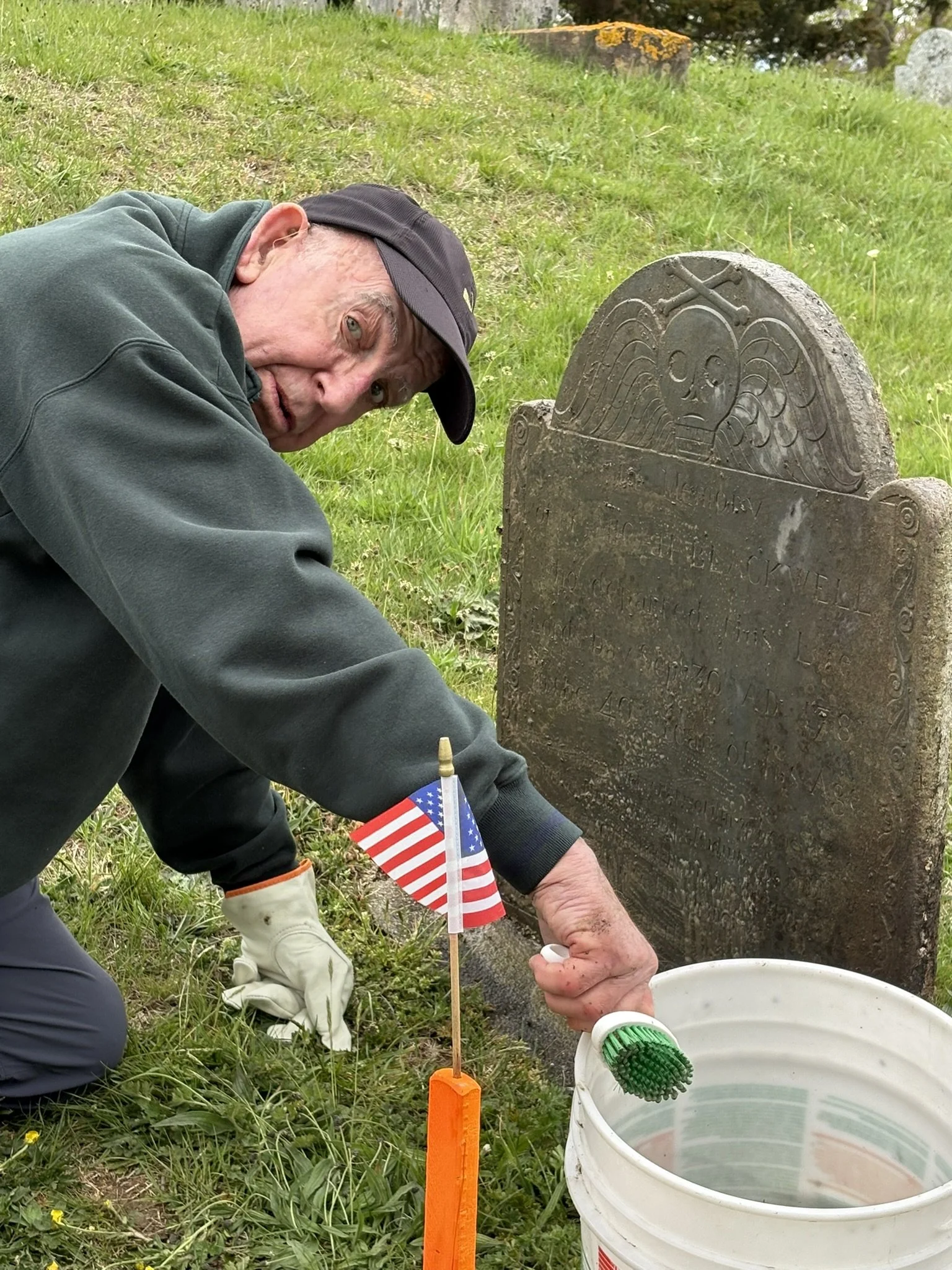 A direct descendent cleans the headstone of ancestor Micah Blackwell in Old Town Cemetery, Sandwich