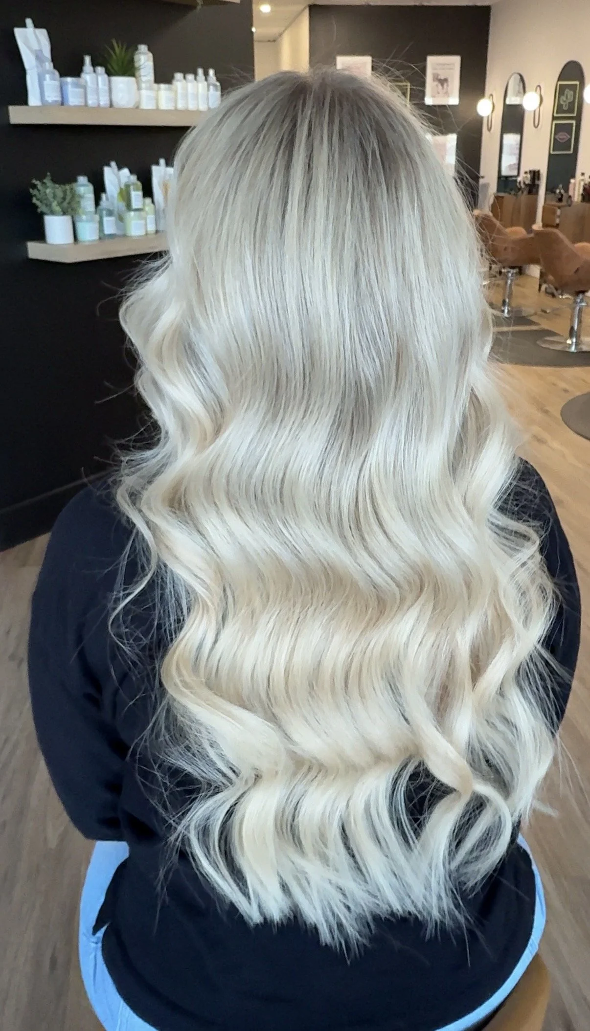 Back of a person with long, platinum blonde, wavy hair sitting in a salon.