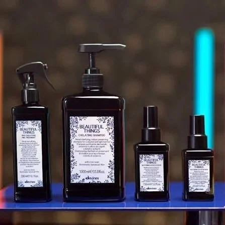 Four black bottles of various sizes with white labels, containing beauty or hair care products, displayed on a blue surface with a blurred background.