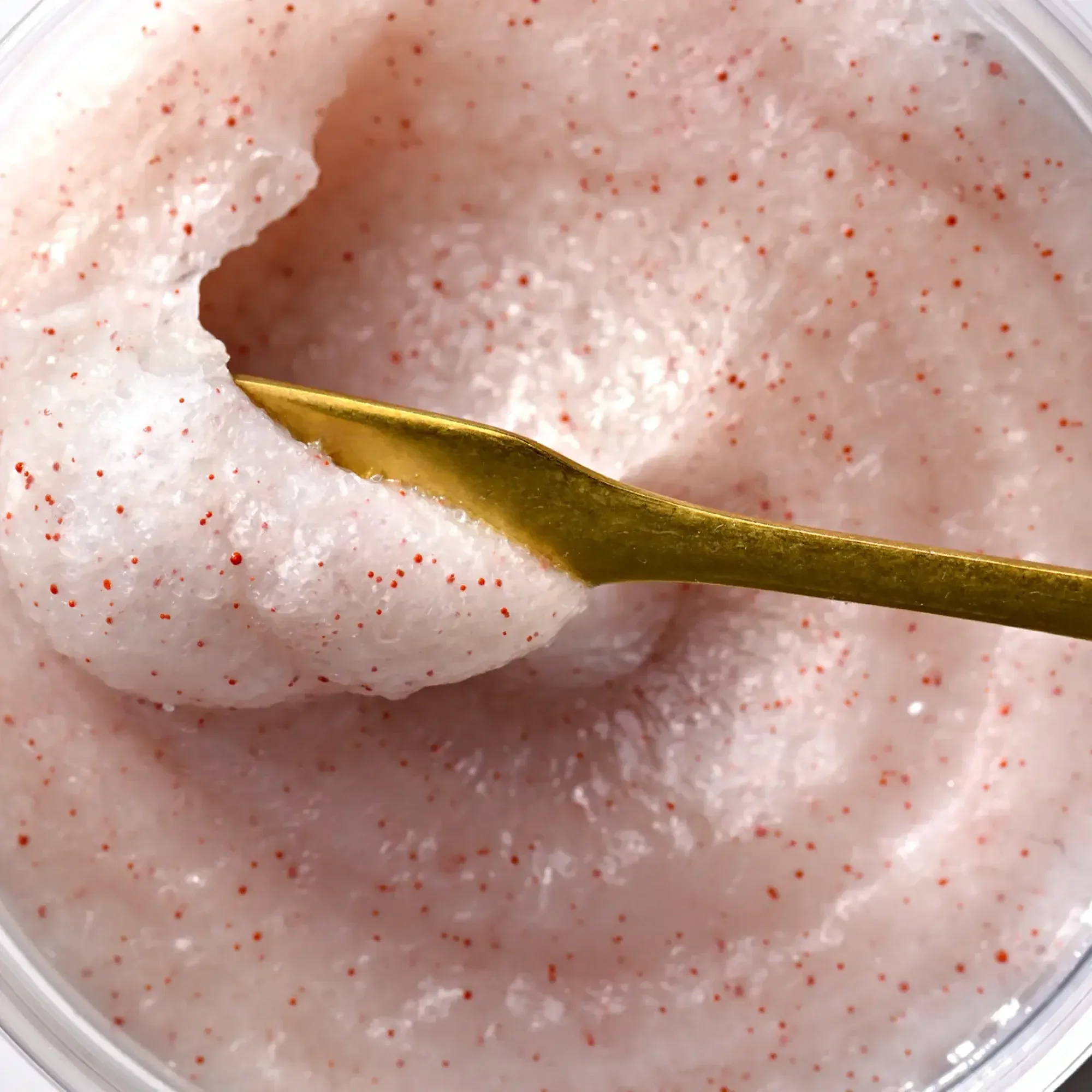 Close-up image of a pink, fluffy, whipped dessert with red sprinkles, with a gold spoon resting on it.