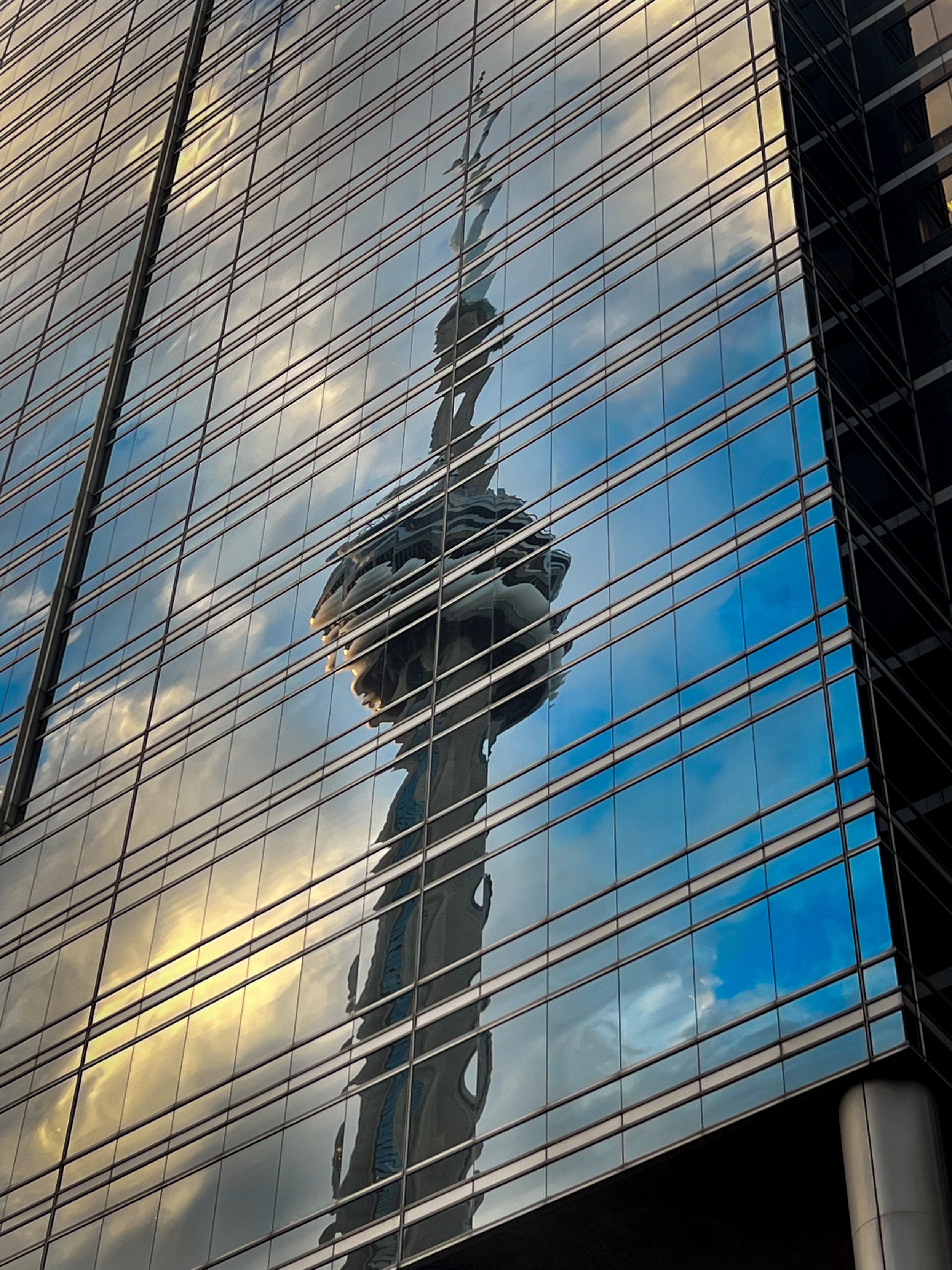 Reflection of a person taking a photo in a glass building with clouds and sky reflected on the glass.