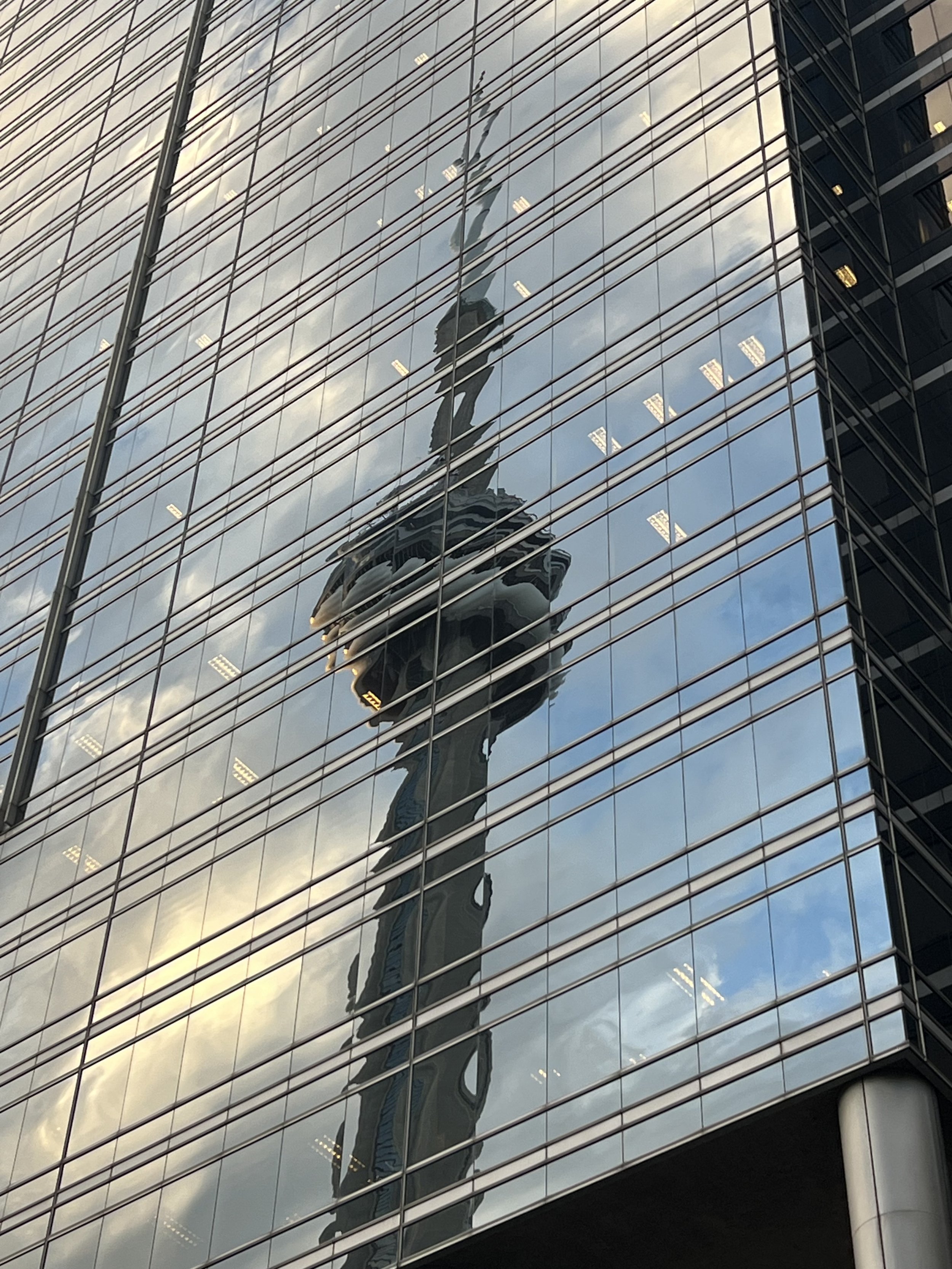 Reflection of a woman on glass building windows, with an observation tower in the background.
