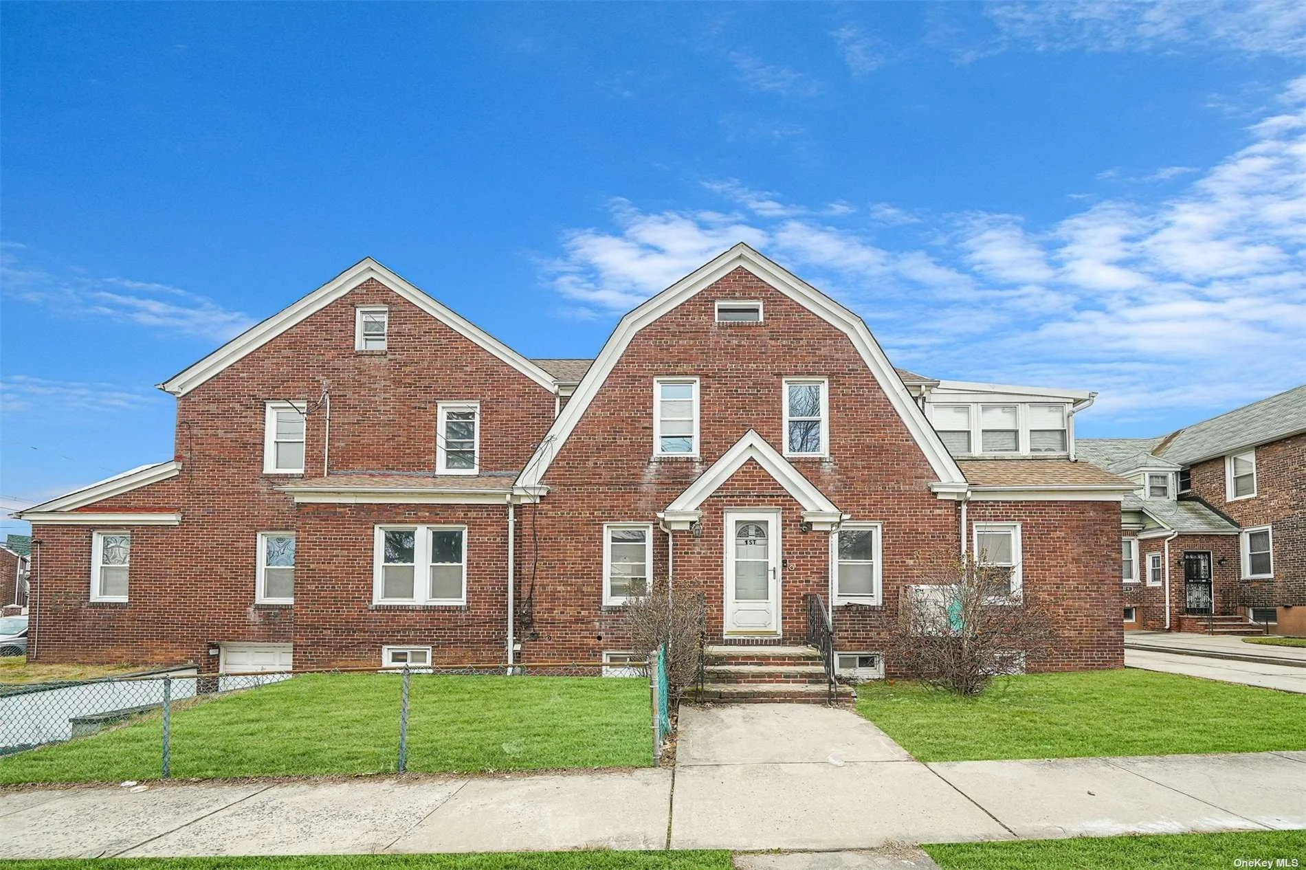 Brick house with multiple windows, small front porch stairs, and a well-maintained lawn under a partly cloudy blue sky