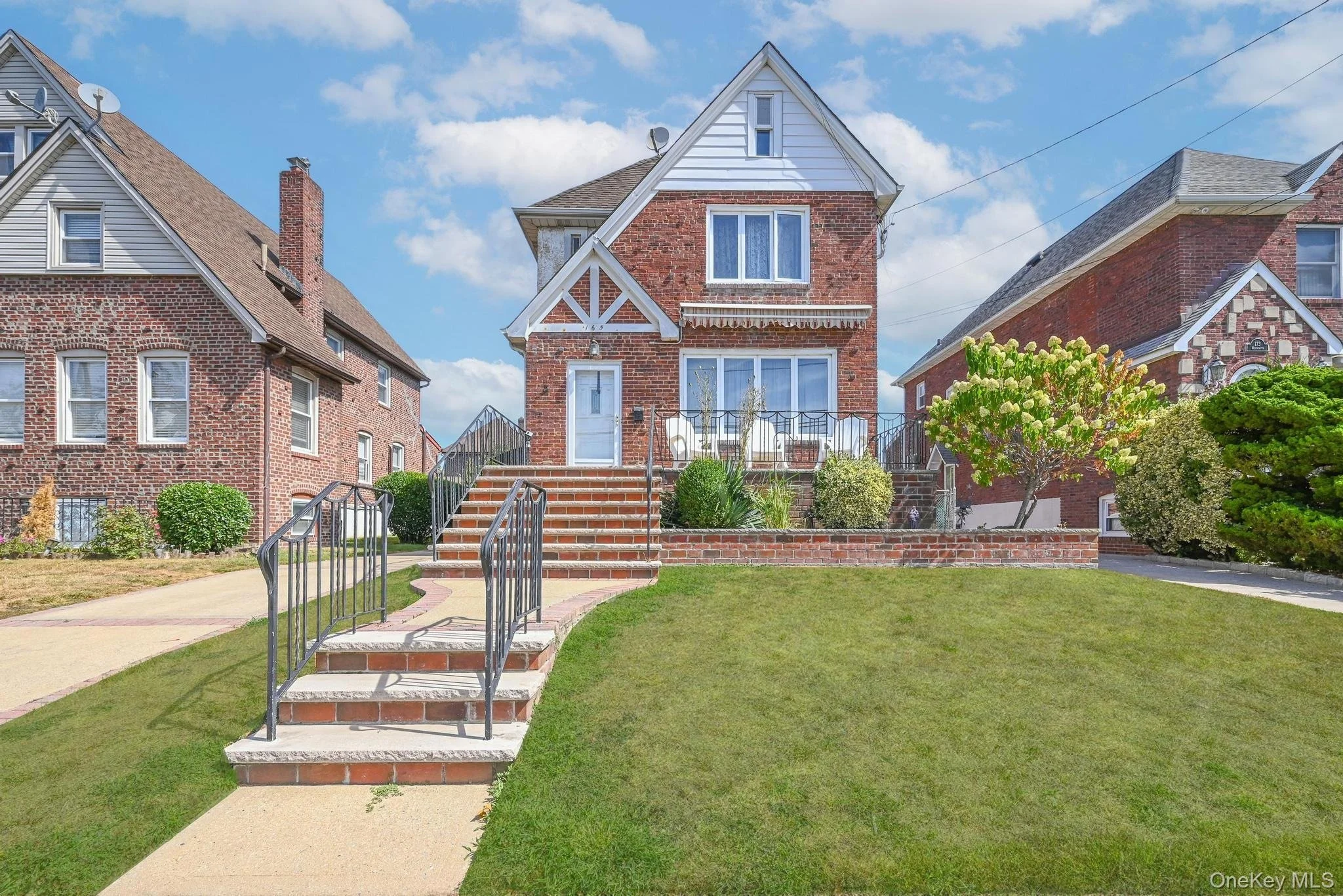 A brick house with a front porch, stairs, and a well-maintained lawn under a partly cloudy sky.