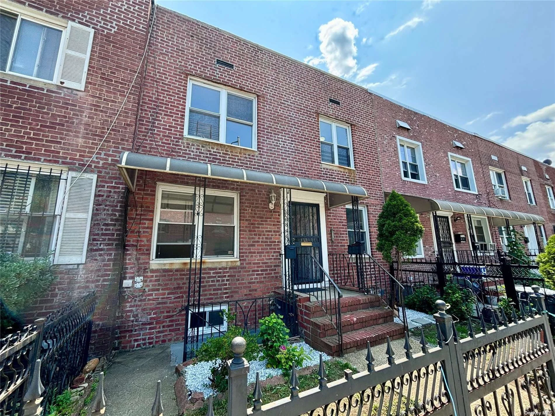 Row of brick townhouses with small front yards, some with awnings and stairs leading to the front doors, under a partly cloudy sky.
