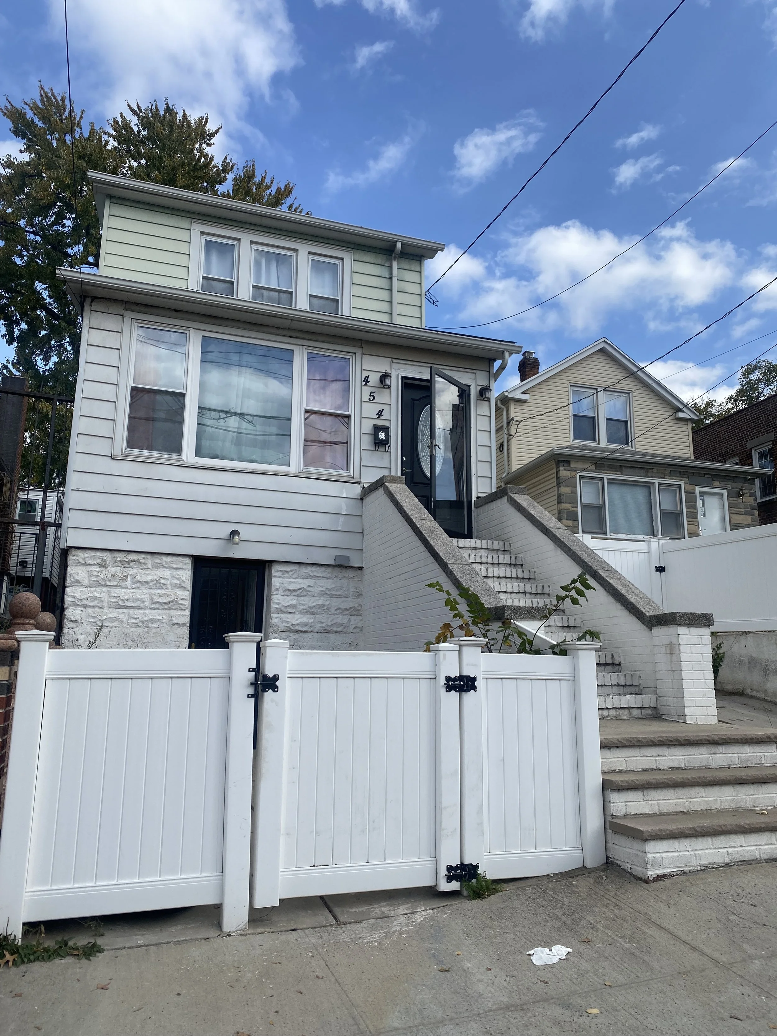A three-story house with a white fence and staircase leading to the front door.