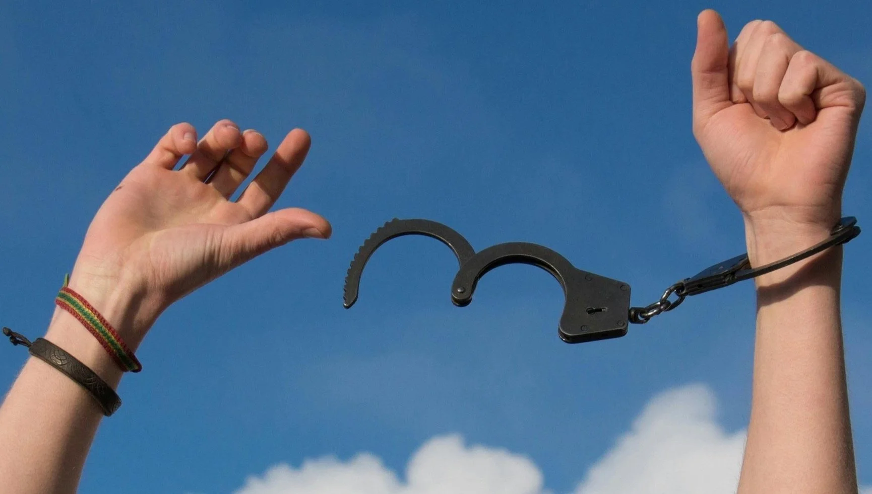 Hands breaking free from open handcuffs against the sky, symbolizing the struggle between independence and connection in intimate relationships.