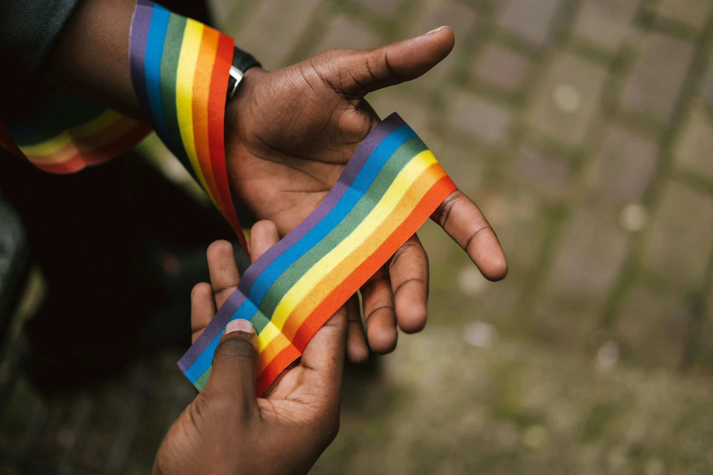 “Close-up of hands holding a rainbow Pride ribbon, symbolizing LGBTQ+ identity and support.”