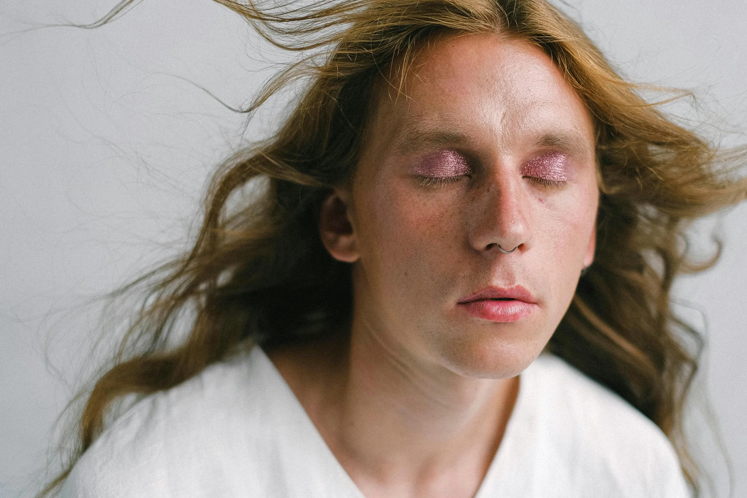 A person with soft expression and glittery eyelids, symbolizing the vulnerability and resilience involved in facing microaggressions toward gender identity.